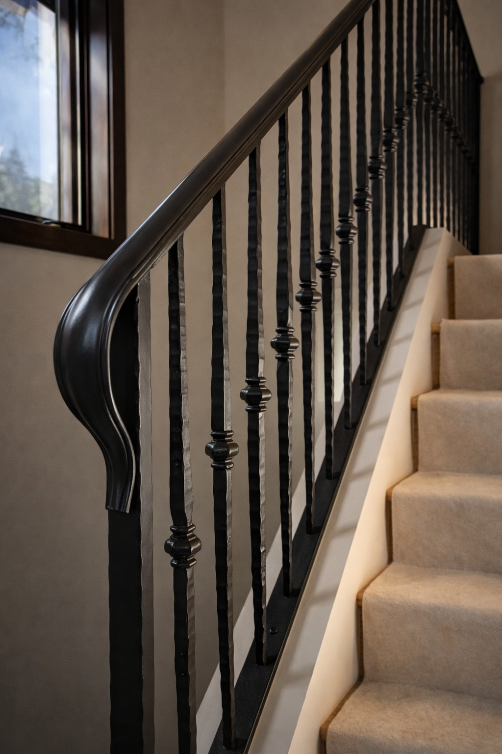 Beautiful wrought iron powder coated metal railing on a staircase next to beige carpeted stairs and a window with a wooden frame.