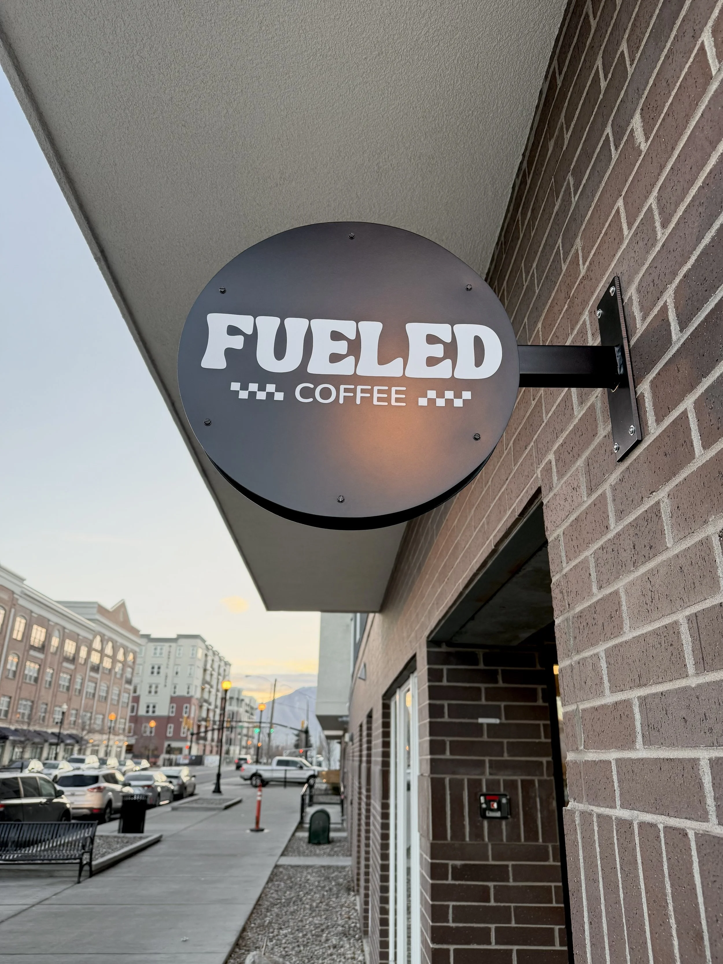 Outdoor sign for Fuled Coffee hanging on brick wall of a building
