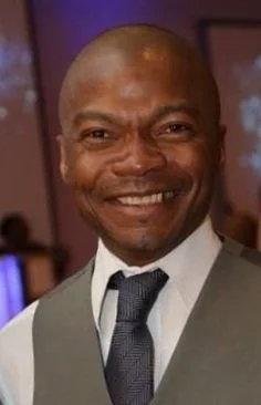 Man smiling in formal attire at an indoor event.