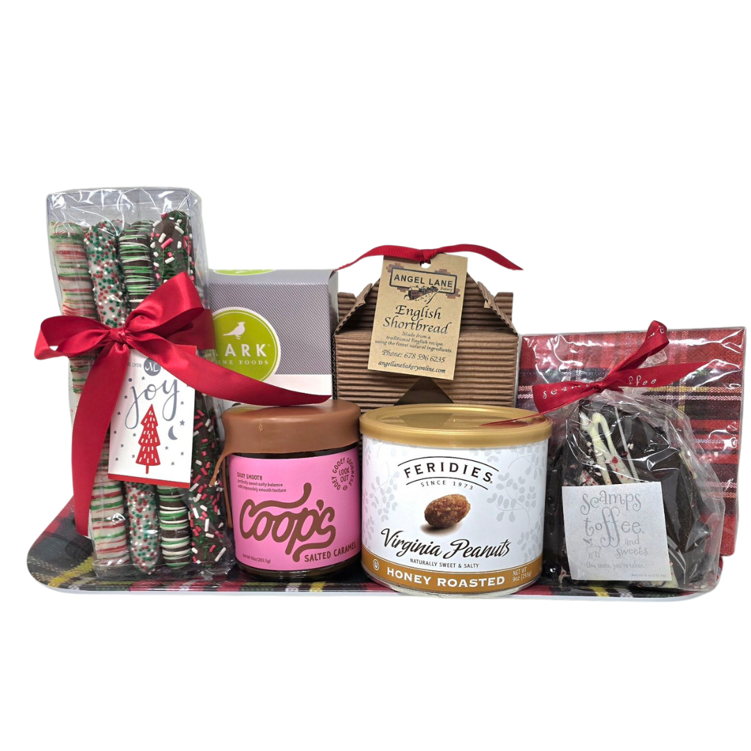 Festive holiday gift tray with assorted treats including candy canes, a box of assorted chocolates, a jar of salted caramel cookie butter, a container of honey roasted Virginia peanuts, and a bag of coffee and sweets, all decorated with red ribbons and holiday tags.