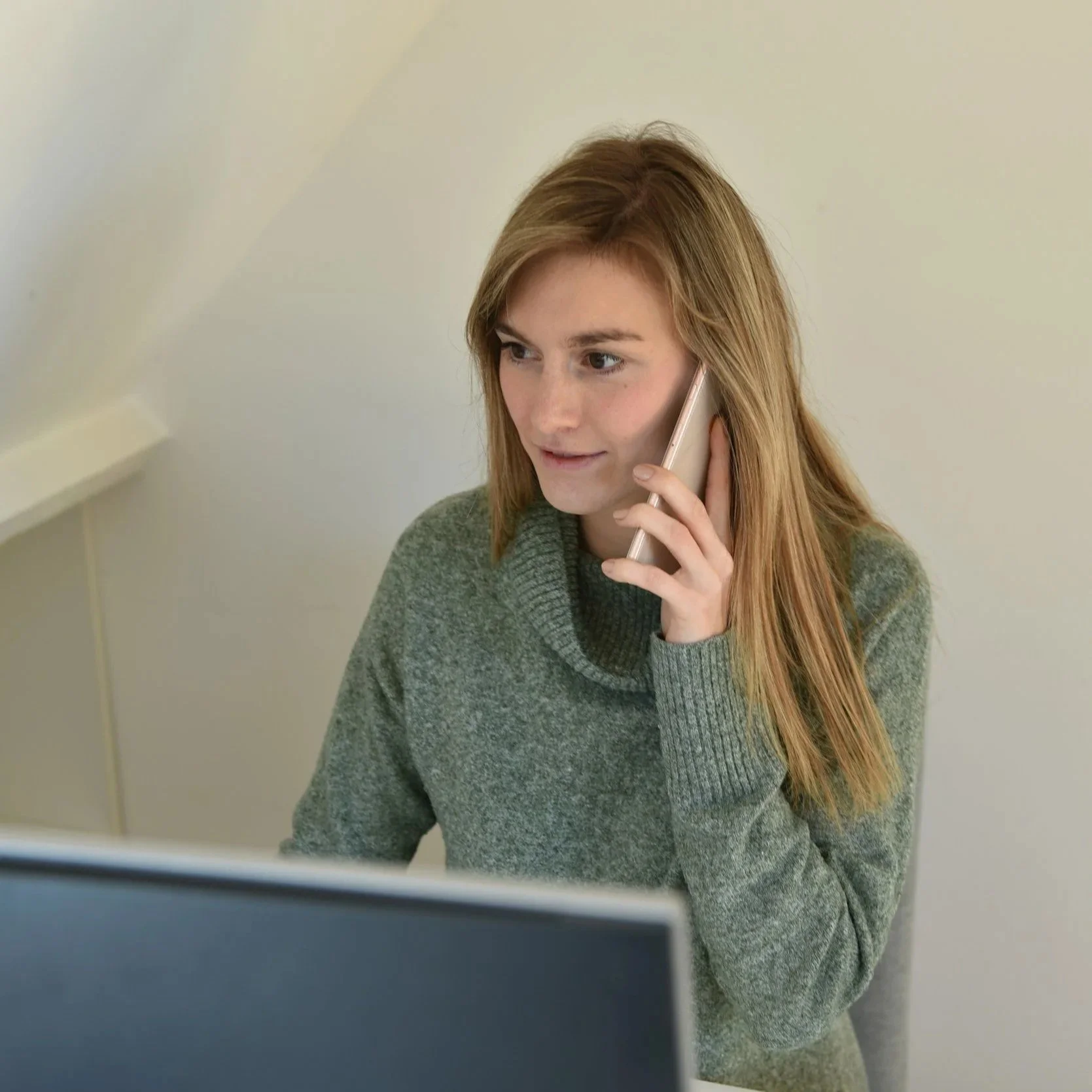 A woman with long red hair wearing a green sweater talking on a landline phone.