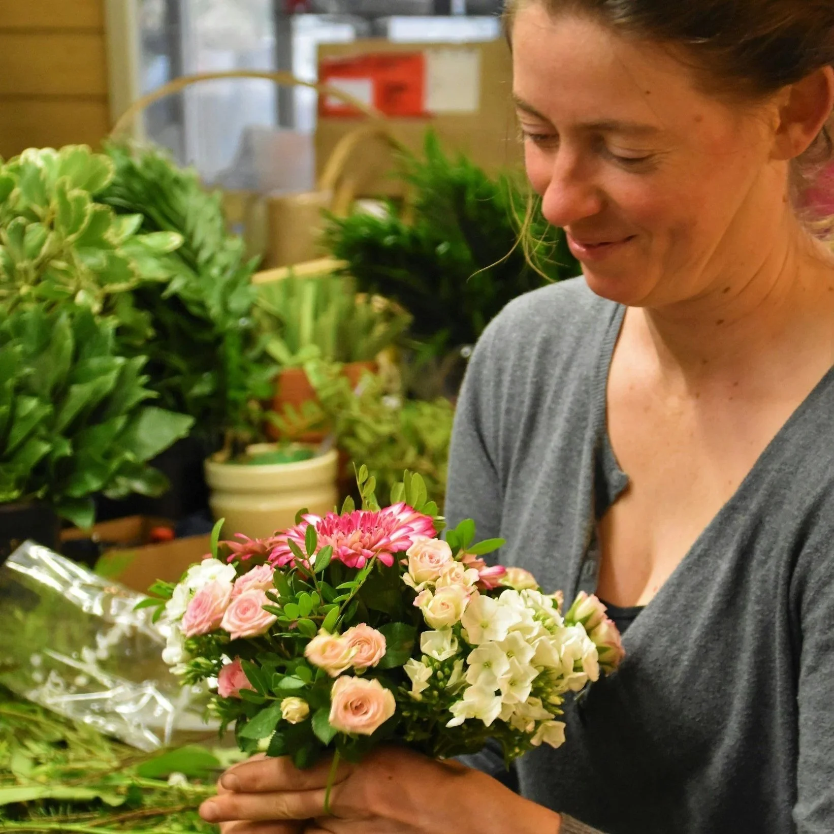 A woman with light skin holding a bouquet of pink and cream roses and other flowers in a flower shop.