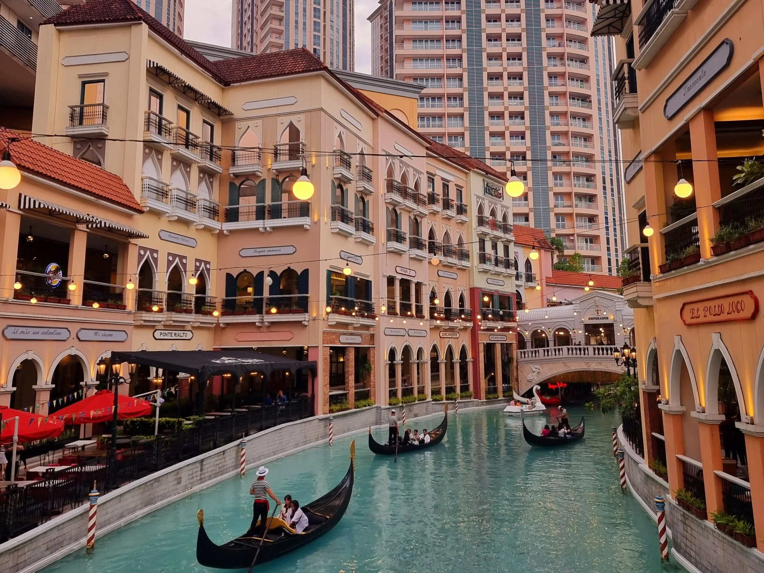 A picturesque canal with gondolas gliding through aqua water, bordered by Venetian-style buildings adorned with lights, evokes a serene and romantic ambiance.