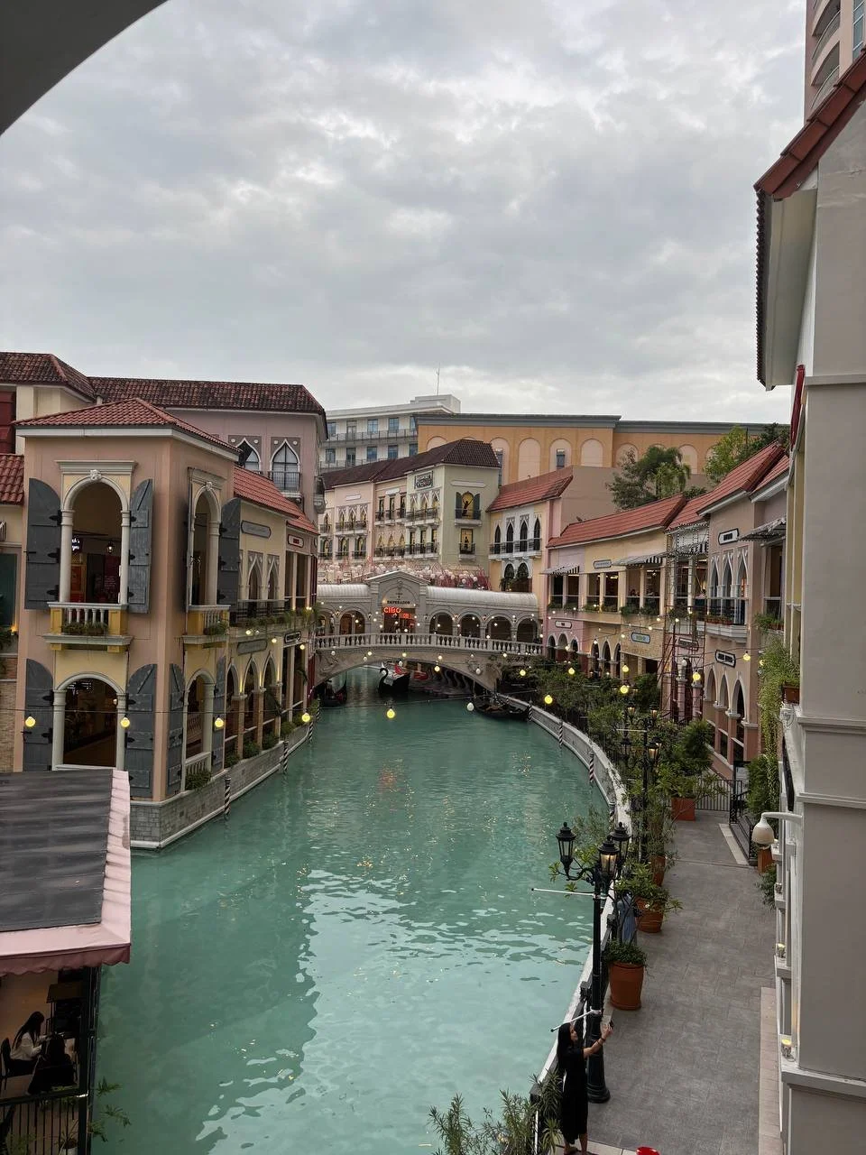 Scenic view of a canal with colorful European-style buildings lining the water, a small bridge crossing over the canal, and an overcast sky.