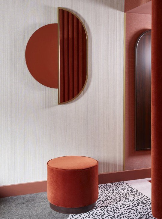 Modern interior with abstract wall art, round red stool, and geometric design elements on a textured wall.