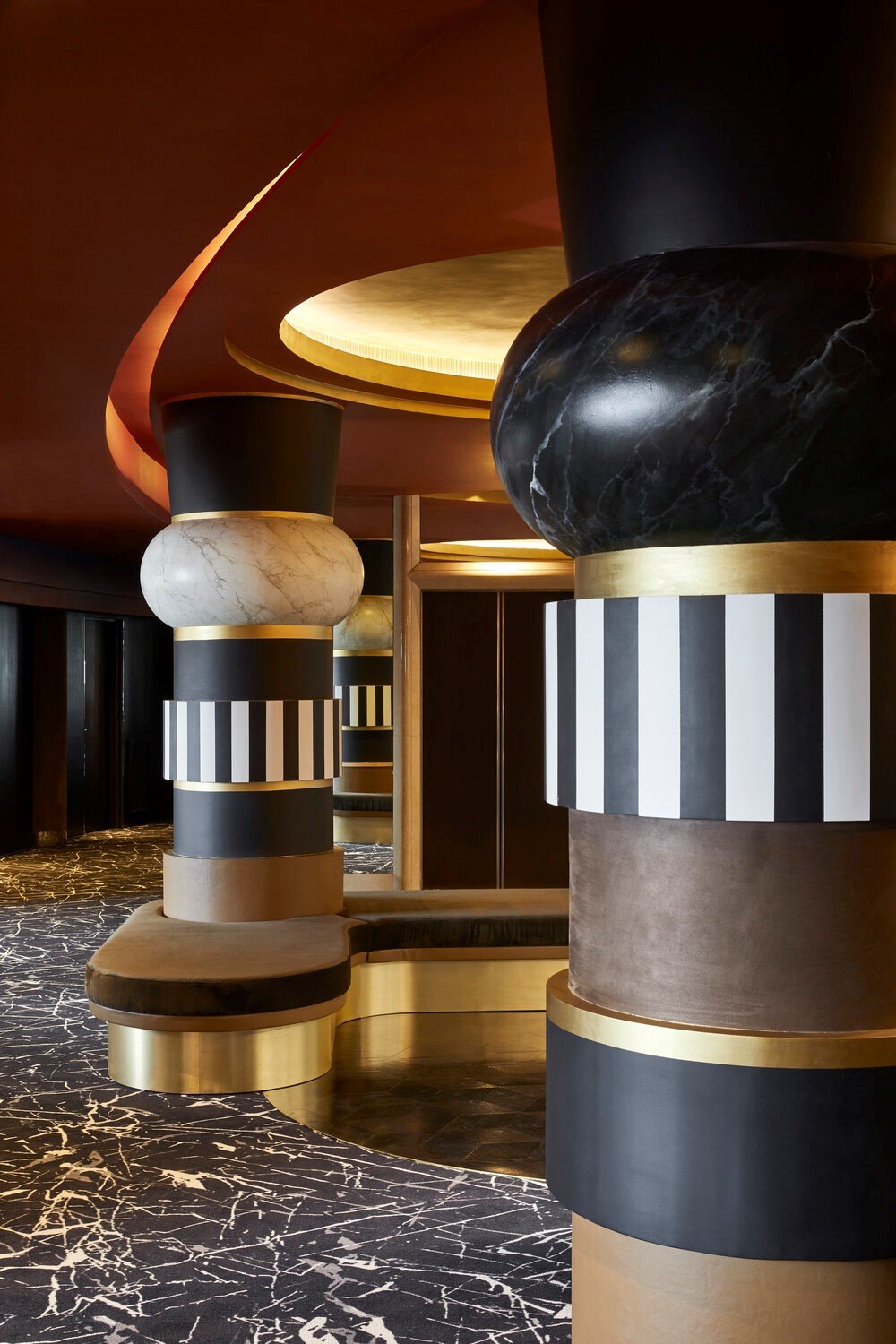 Modern interior design featuring black and white striped columns with gold accents, a marble-patterned floor, and curved ceiling elements.