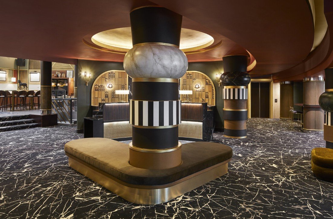 Luxury hotel lobby with modern art deco design featuring round columns, patterned carpet, and elegant lighting.
