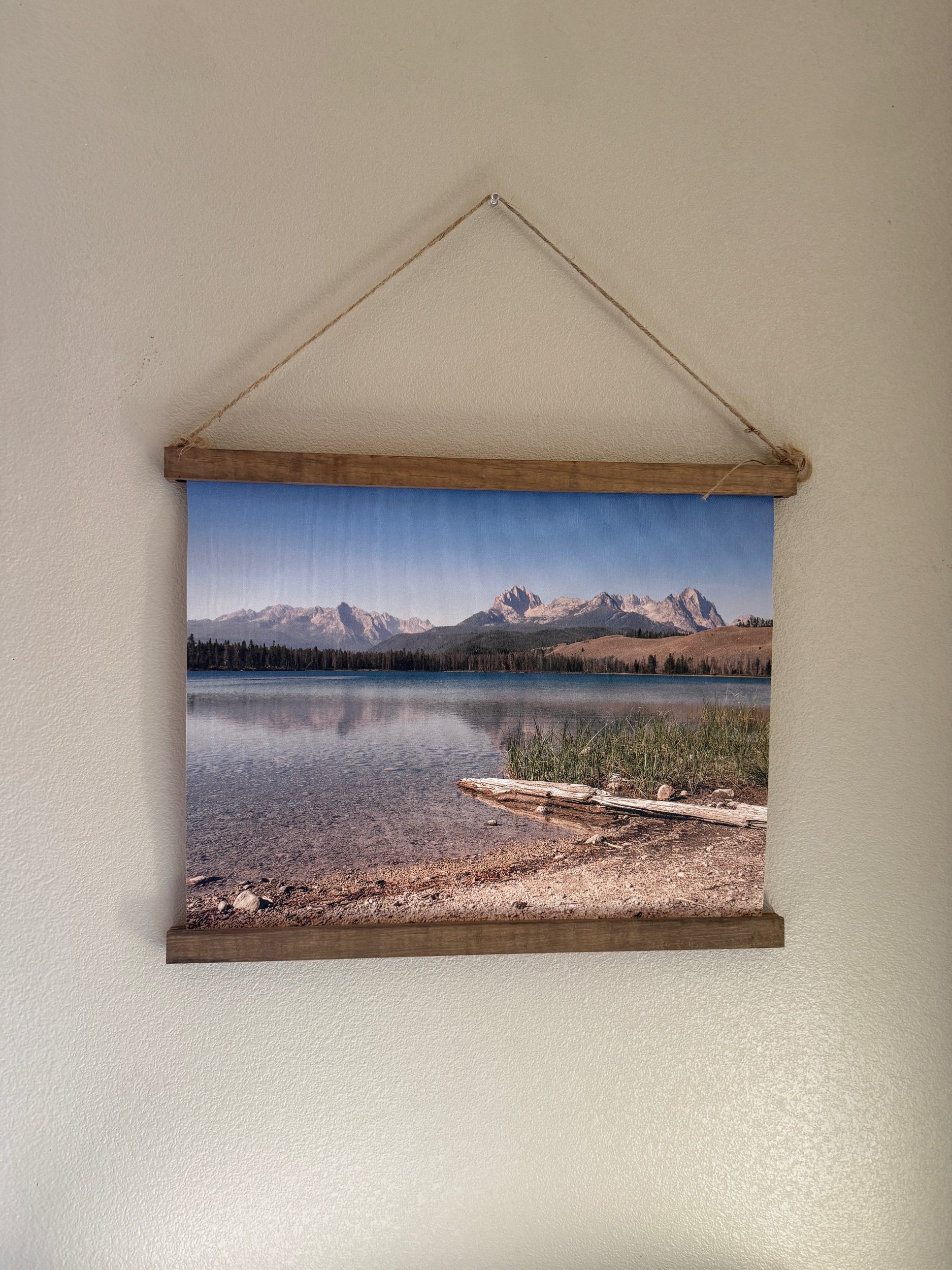 Sawtooth Mountains reflected on a calm lake, printed as a canvas wall hanging with natural wood rails and jute twine.