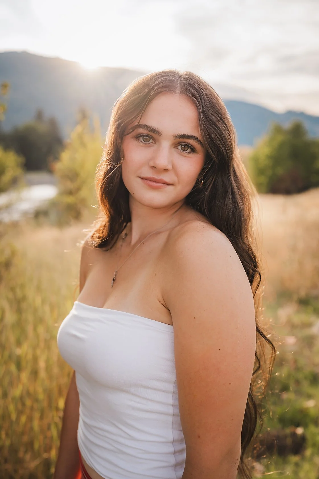 Eagle High School senior girl in a white top standing in a golden field with mountains and sunset light behind her in Garden Valley Idaho