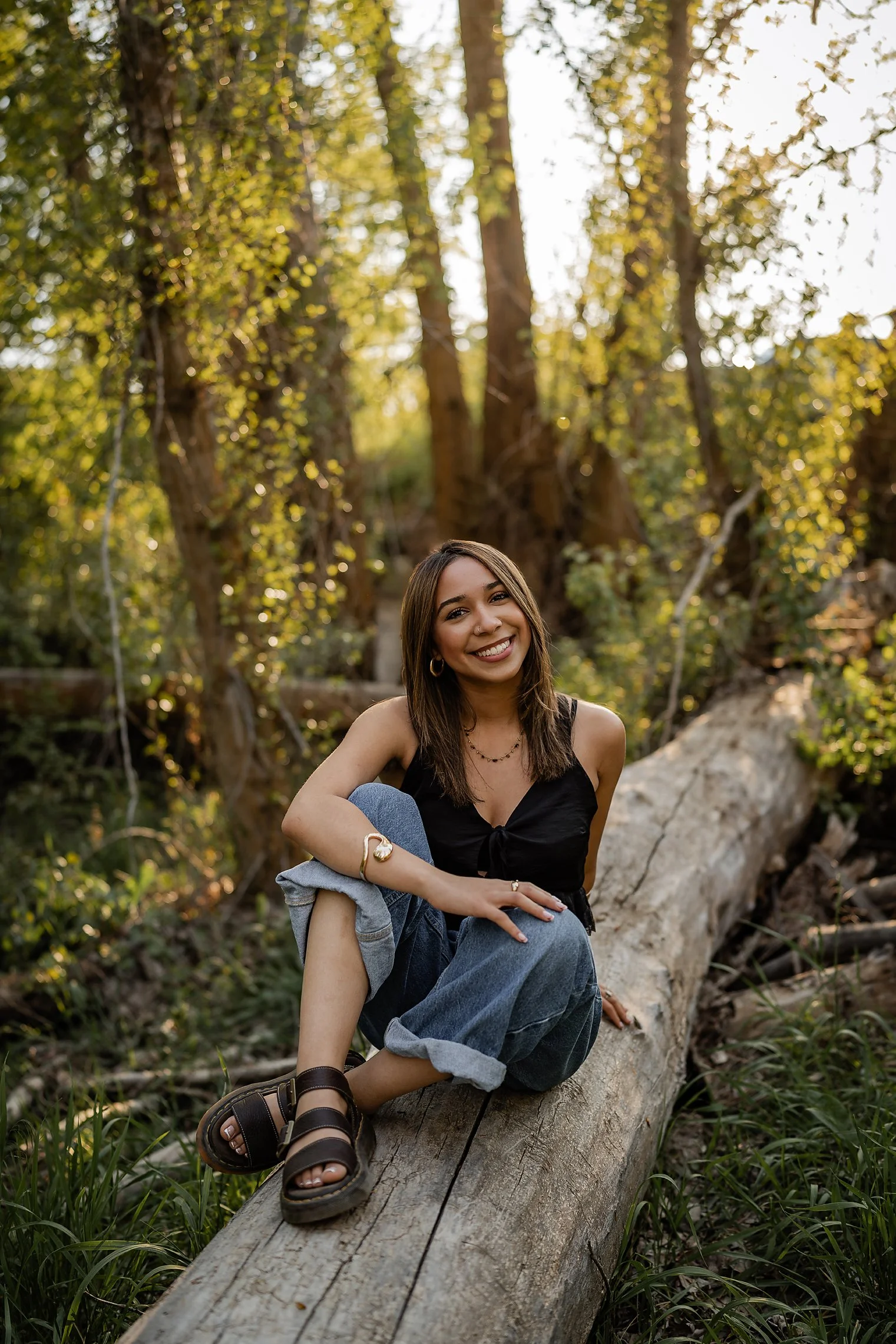 High school senior sitting on a fallen log in a sunlit forest during golden hour, Nampa Idaho senior photography