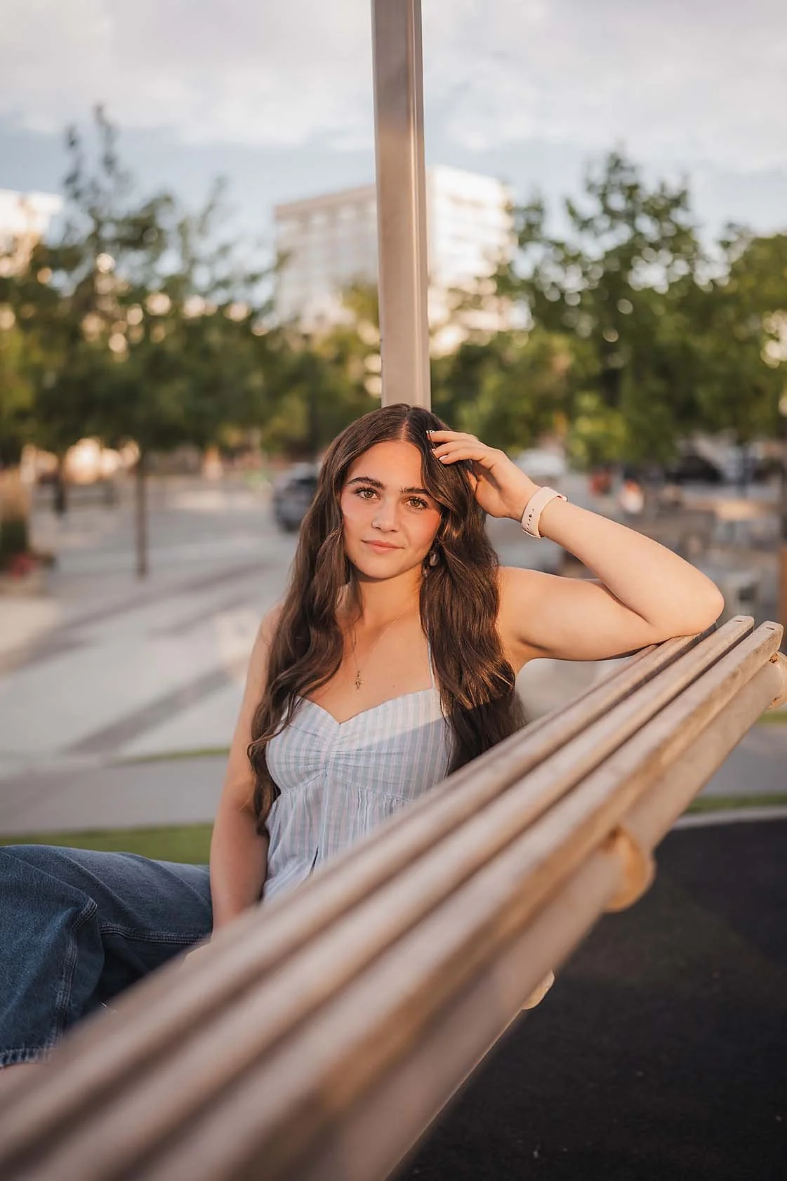 Eagle High School senior girl in a blue top sitting on a wooden bench in a downtown Boise Idaho park during her senior session