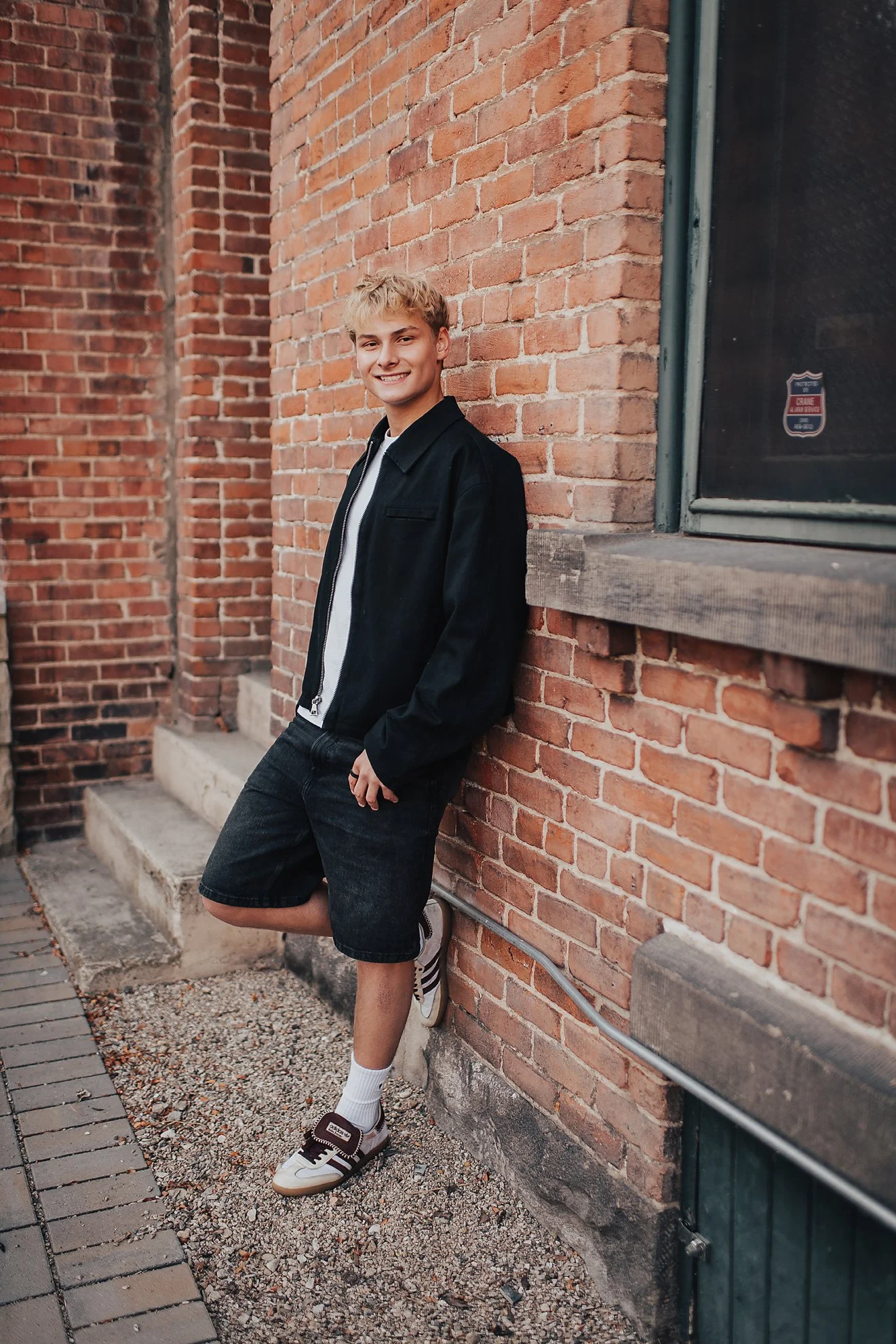 High school senior leaning casually against a brick wall during a comfortable senior session in Boise, Idaho