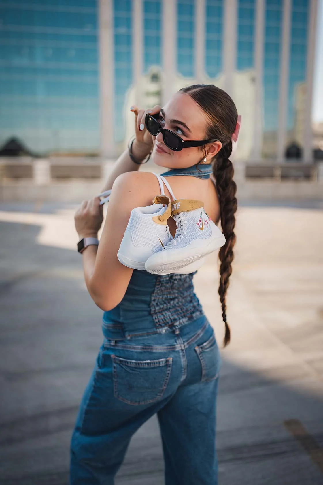 Eagle High School senior wrestler in overalls and sunglasses glancing over her shoulder while holding her wrestling shoes in downtown Boise Idaho