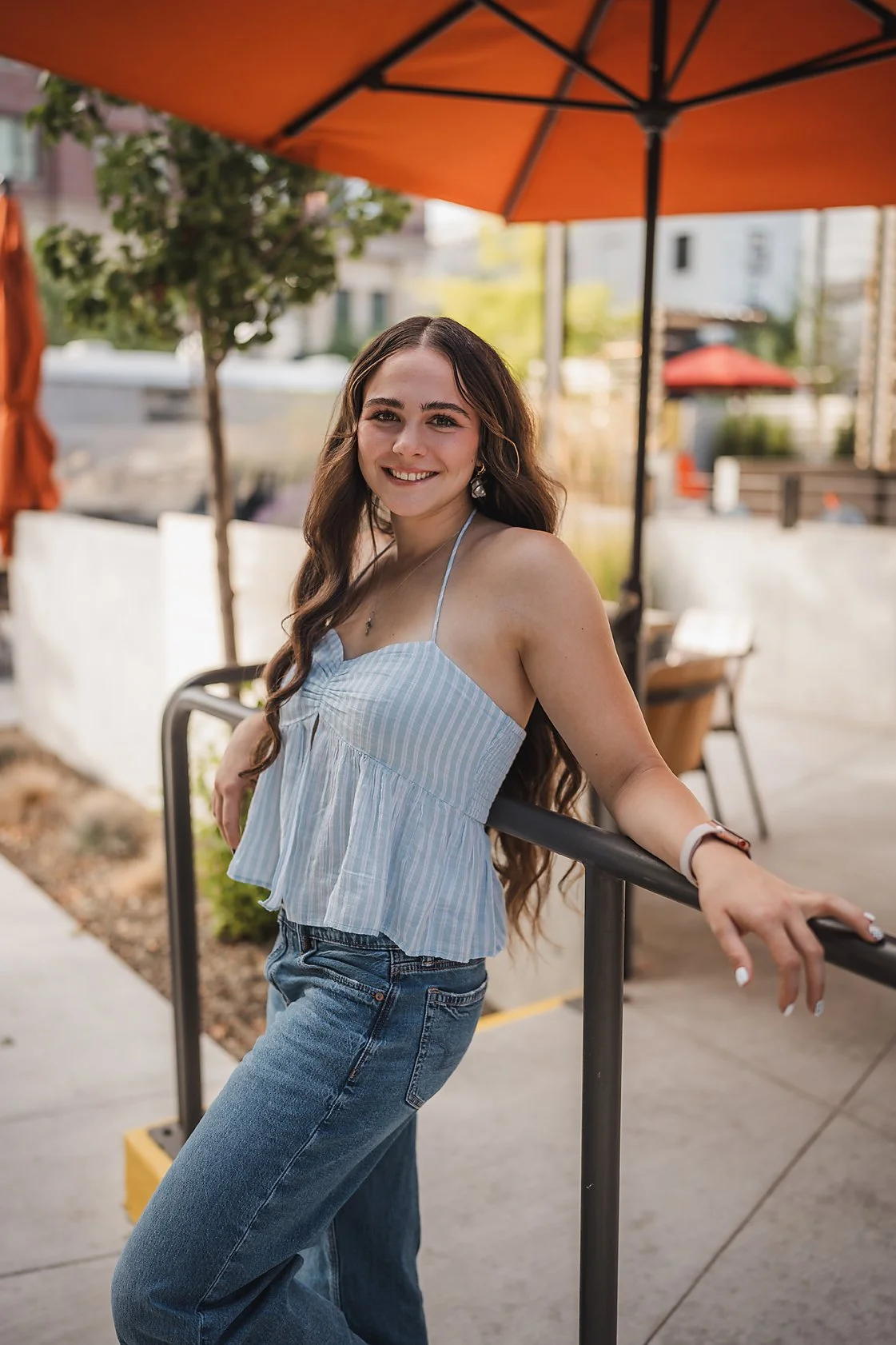 Eagle High School senior girl smiling and leaning on a railing under an orange cafe umbrella in downtown Boise Idaho during her senior session