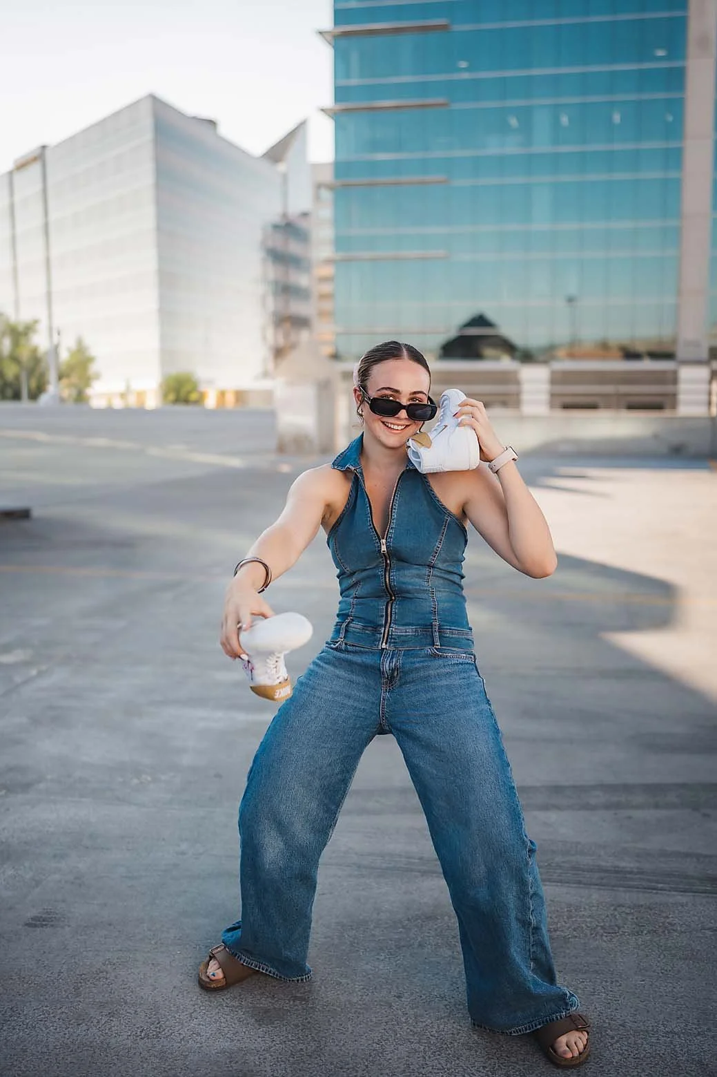 Eagle High School senior wrestler with a braid and pink bow smiling over her shoulder while holding her custom embroidered wrestling shoes in downtown Boise Idaho