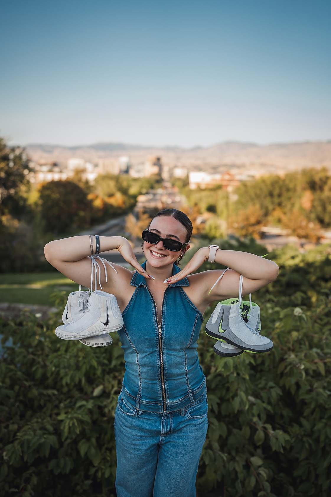 Eagle High School senior wrestler smiling and holding her wrestling shoes over her shoulders with a Boise Idaho city view behind her