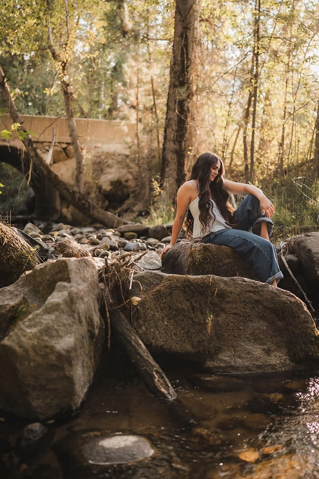 Eagle High School senior girl sitting on mossy rocks beside a creek in a wooded Garden Valley Idaho setting during her senior session