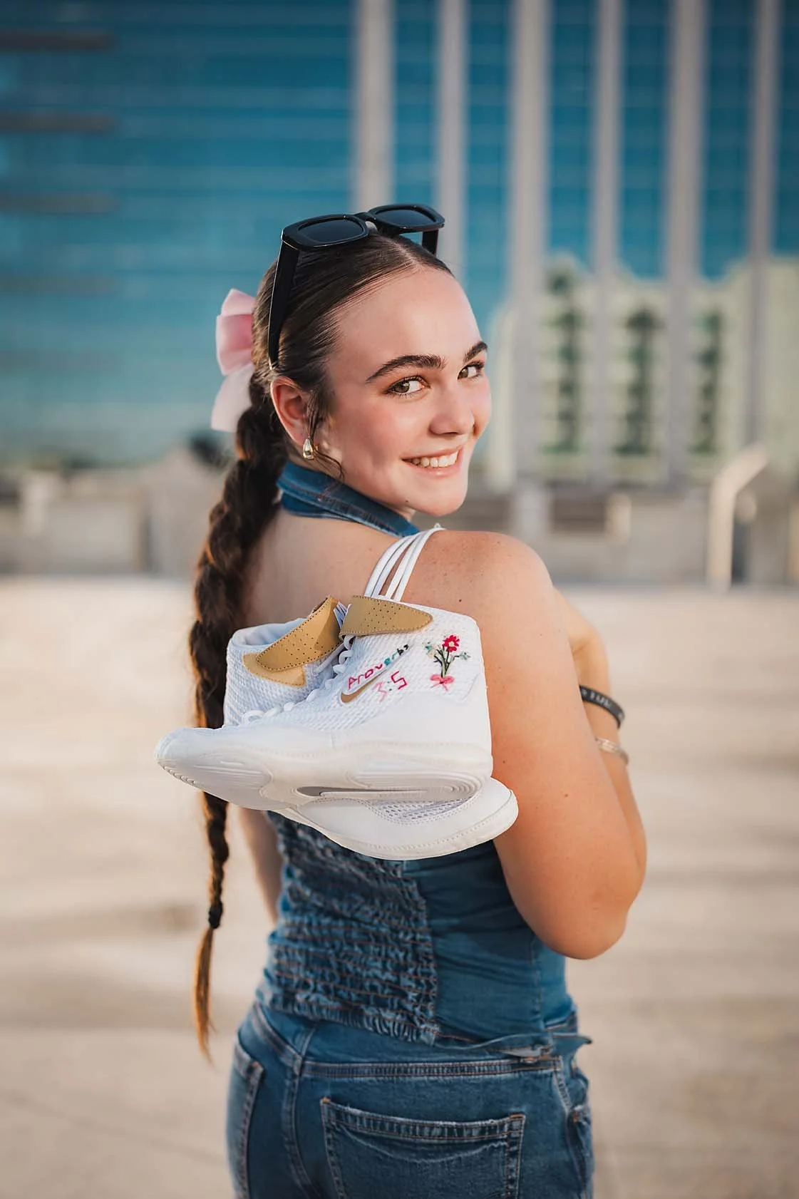 Eagle High School senior wrestler with a braid and pink bow smiling over her shoulder while holding her custom embroidered wrestling shoes in downtown Boise Idaho