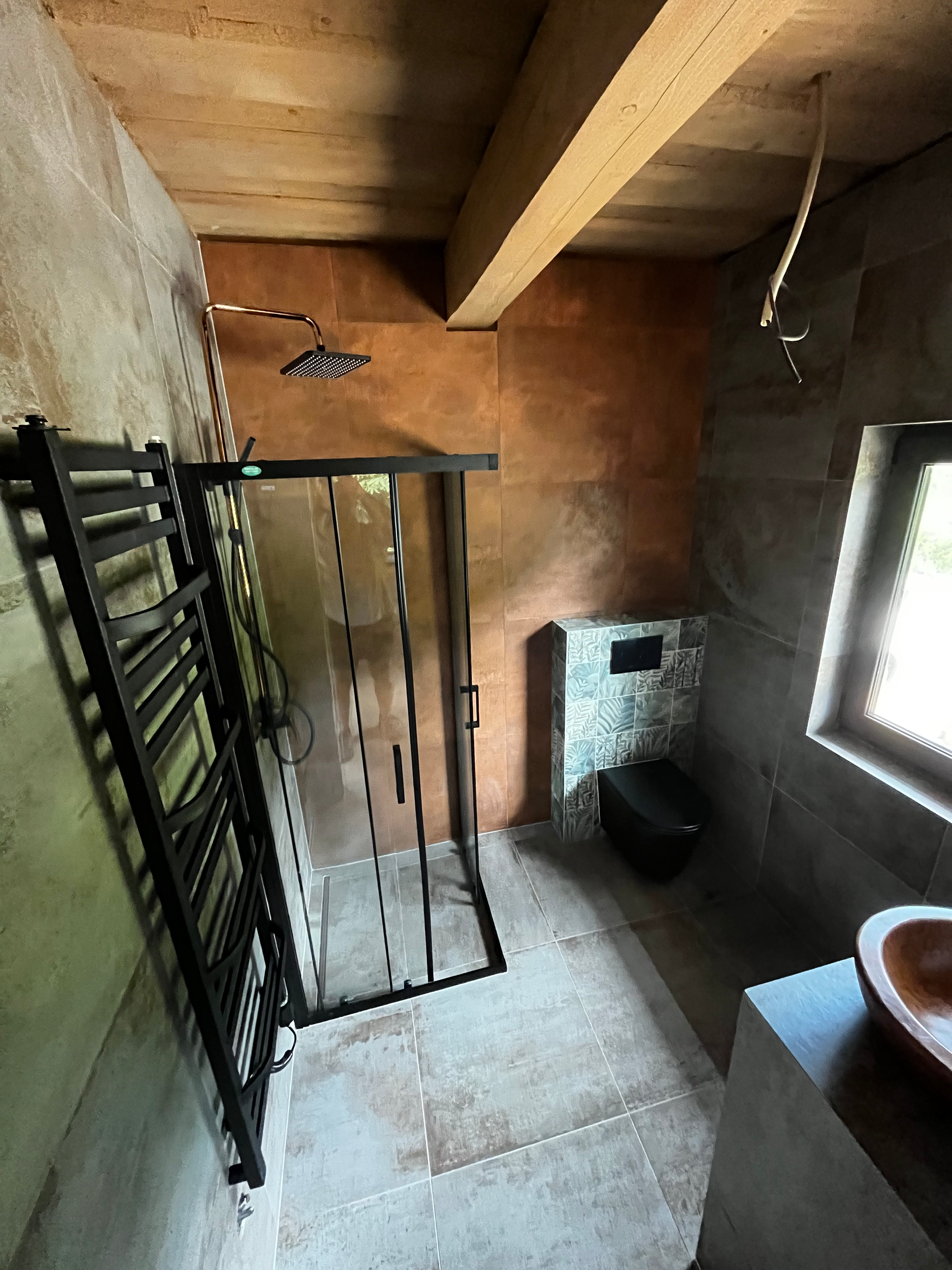 Modern bathroom with walk-in shower with glass door, black heated towel rail, wall-mounted black toilet, window, and sink basin