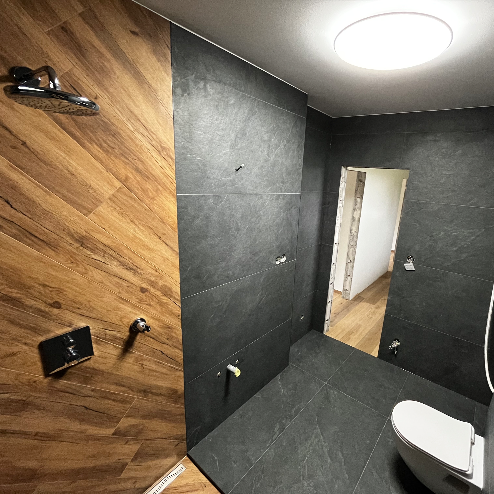 Empty bathroom with dark gray tiled walls and floor, wood-paneled wall, and a modern white toilet.