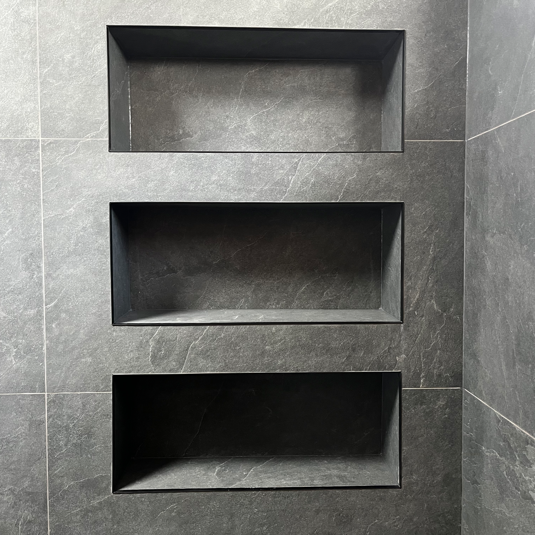 Three rectangular recessed shelves built into a gray tiled wall.