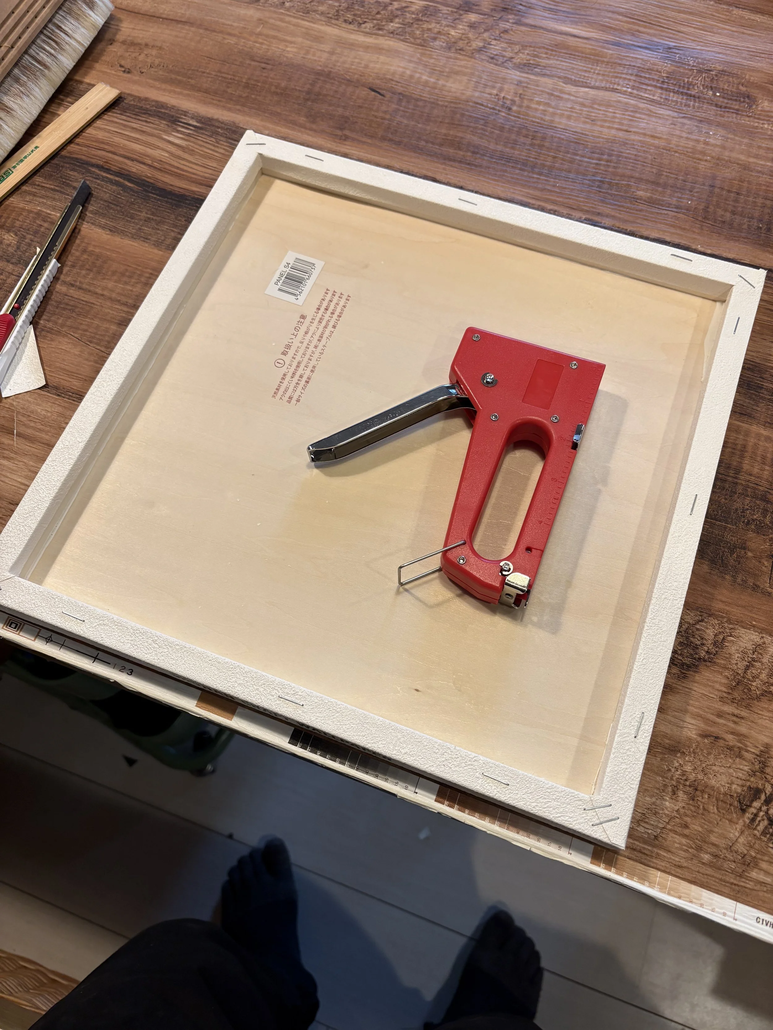 ステープルガンとキャンバスの裏面。作業台にはカッターや刷毛が置かれている。