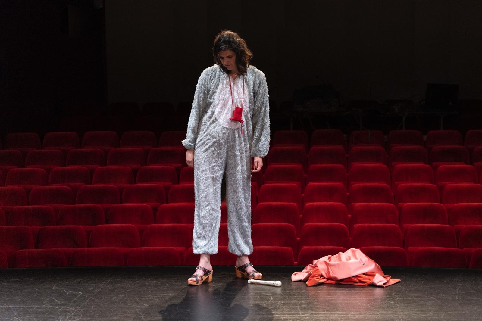 Personne en costume argenté sur scène avec sièges rouges en arrière-plan.