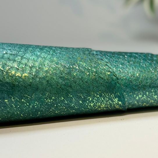 Nahaufnahme einer grünen, gerollten Papierrolle mit goldenen Akzenten auf einer weißen Oberfläche.