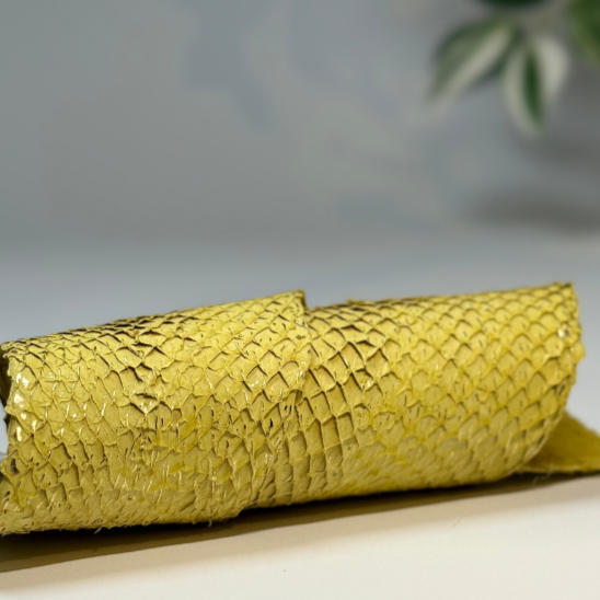Ein goldenes, gefaltetes Taschen- oder Geldbörse aus Schlangenhaut liegt auf einem weißen Tisch, im Hintergrund eine Topfpflanze.