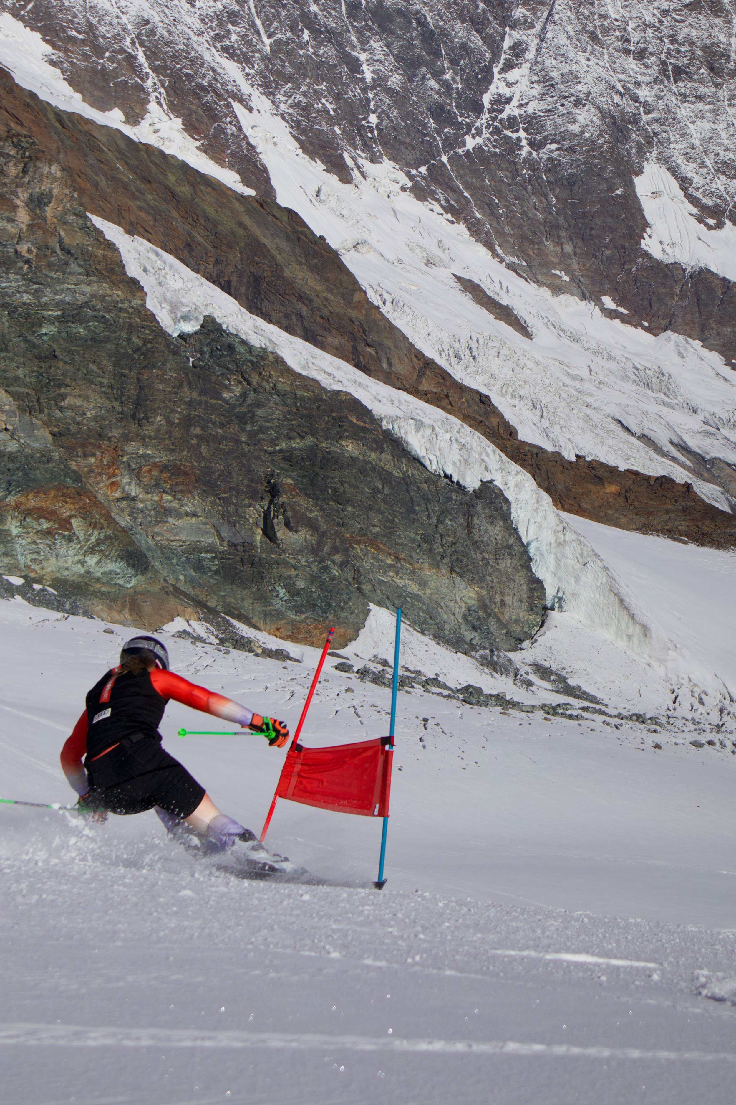 Skifahrer fährt abwärts auf einer Skipiste, passiert ein rotes Tor, umgeben von verschneiten Bergen.