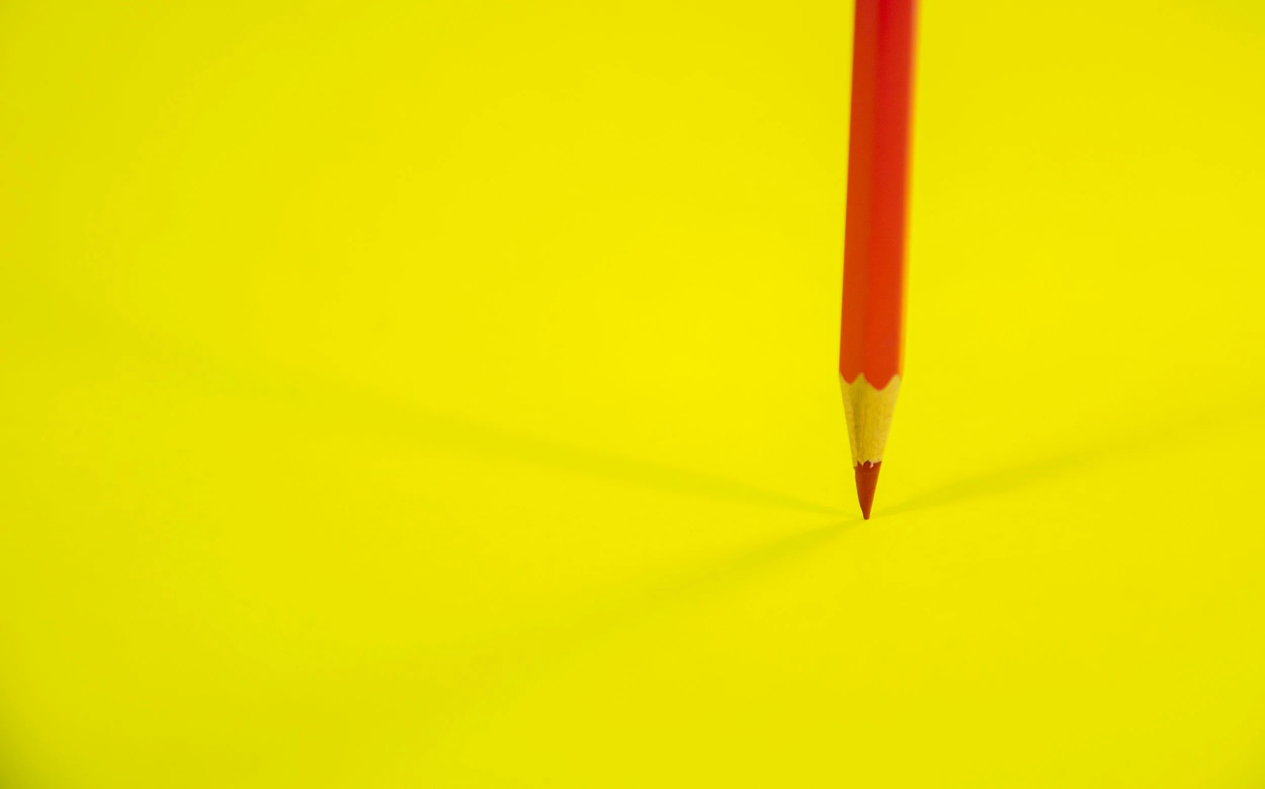 Red colored pencil standing vertically on vibrant yellow background.