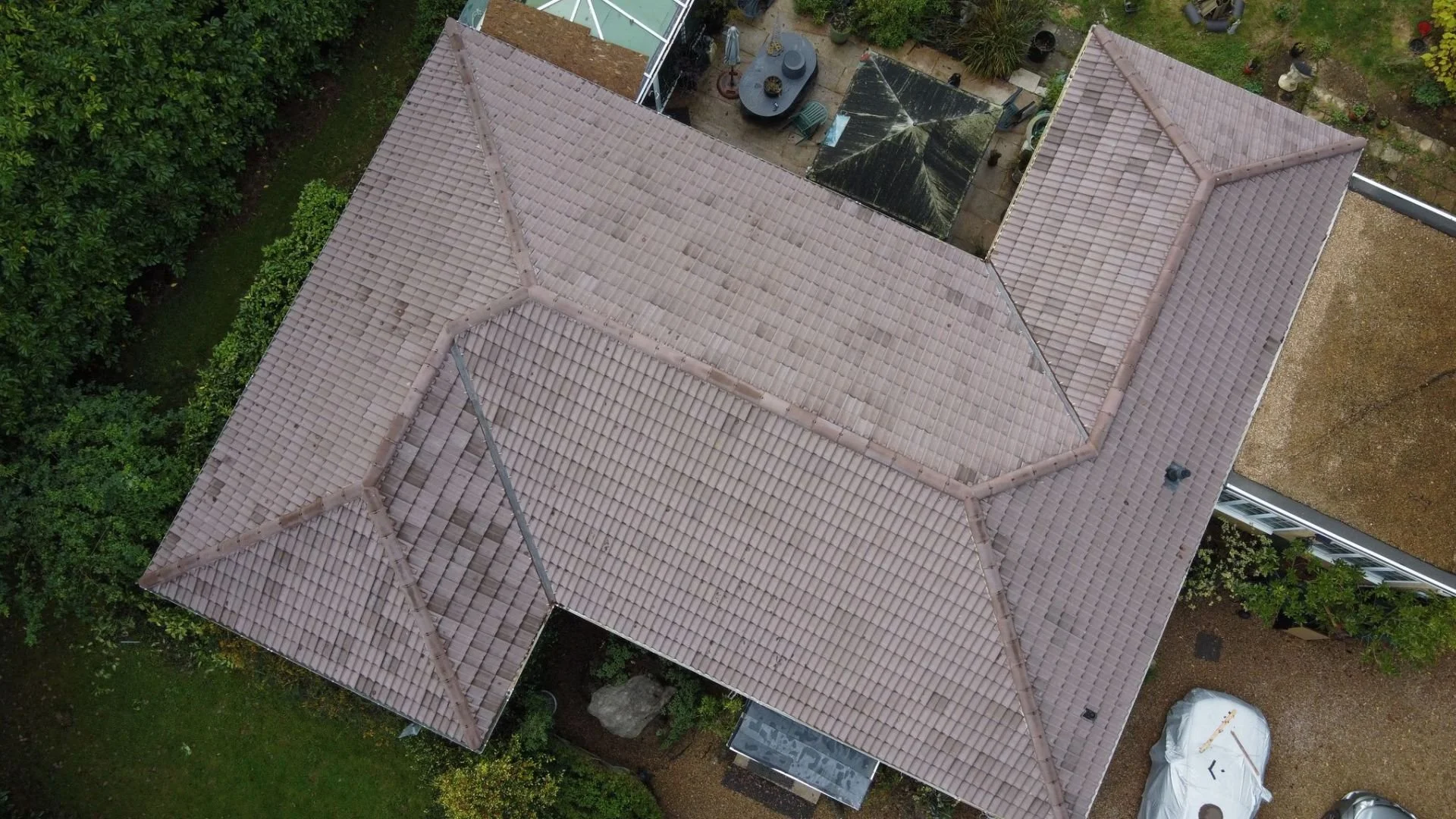 Aerial view of a house's roof with brown tiles and surrounding garden area.