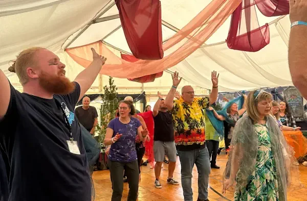 People enthusiastically worshipping in a tent with fabric draped from the ceiling.