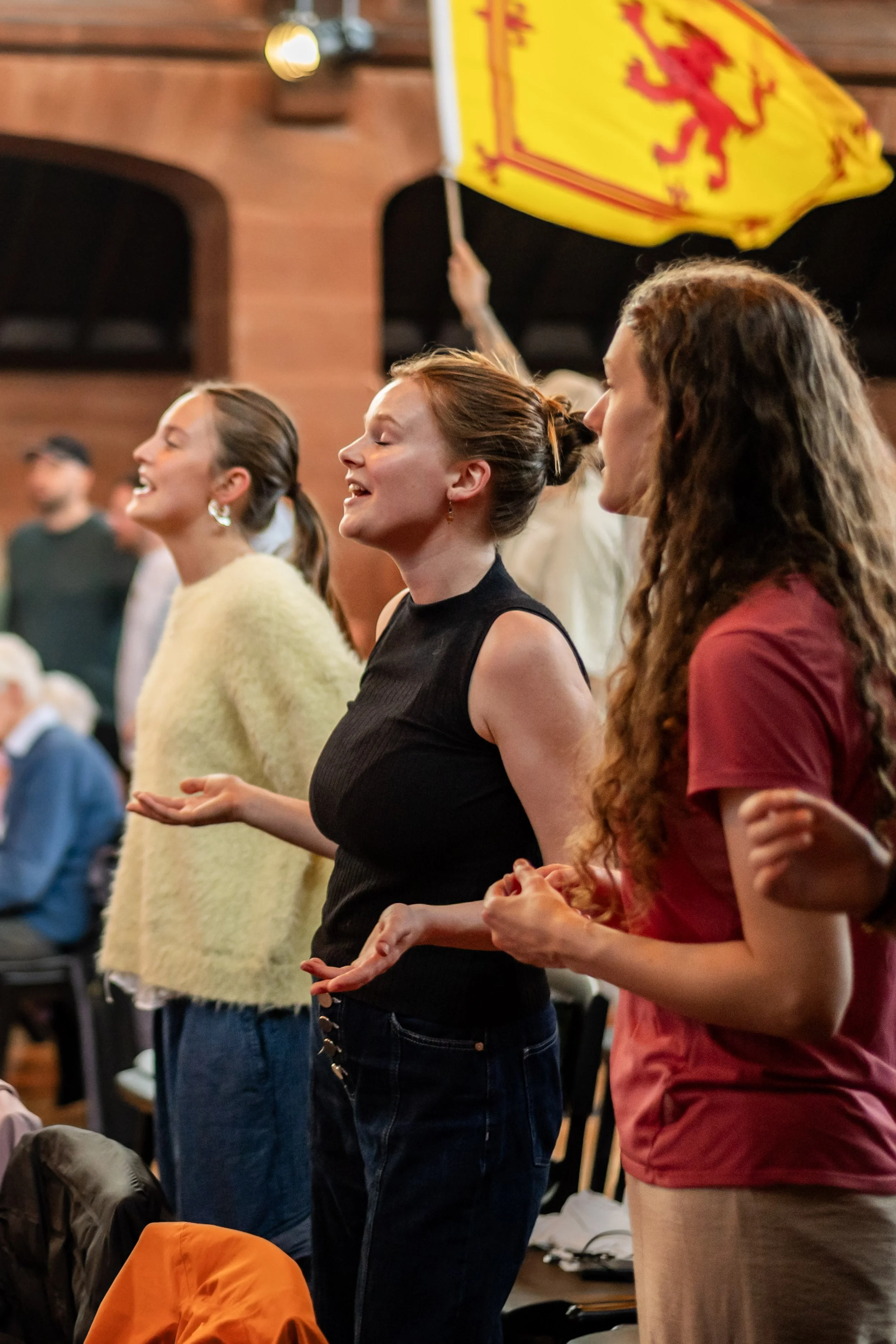 three women worshipping with the Scottish Lion flag in a background.
