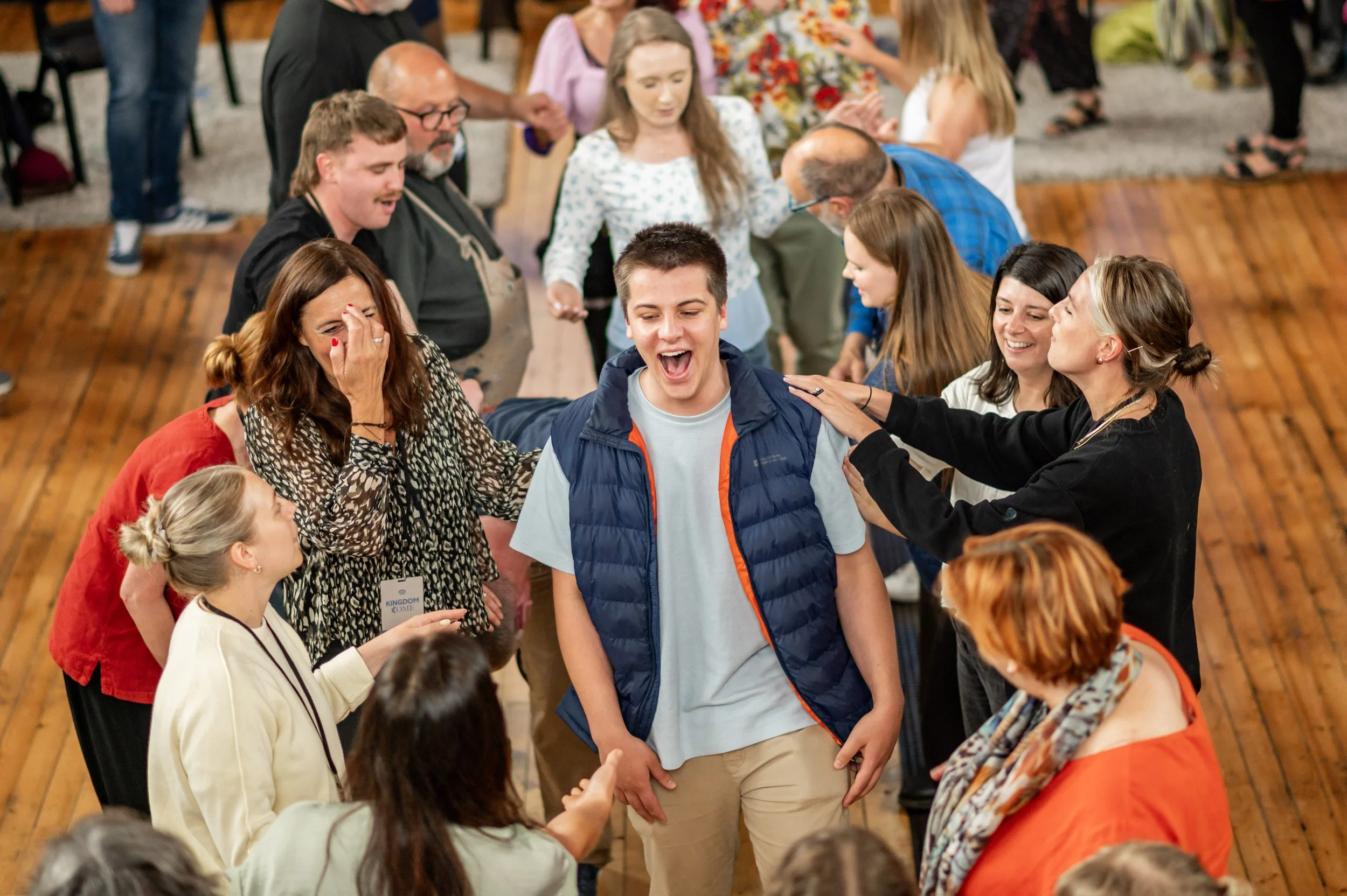 A young man joyously smiling, surrounded by a group of people laying hands on his shoulders and praying for him.