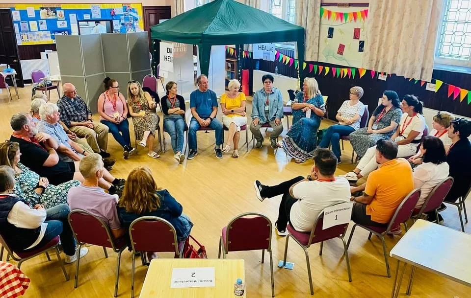 A large group of people sitting in a circle, sharing and talking amongst themselves.