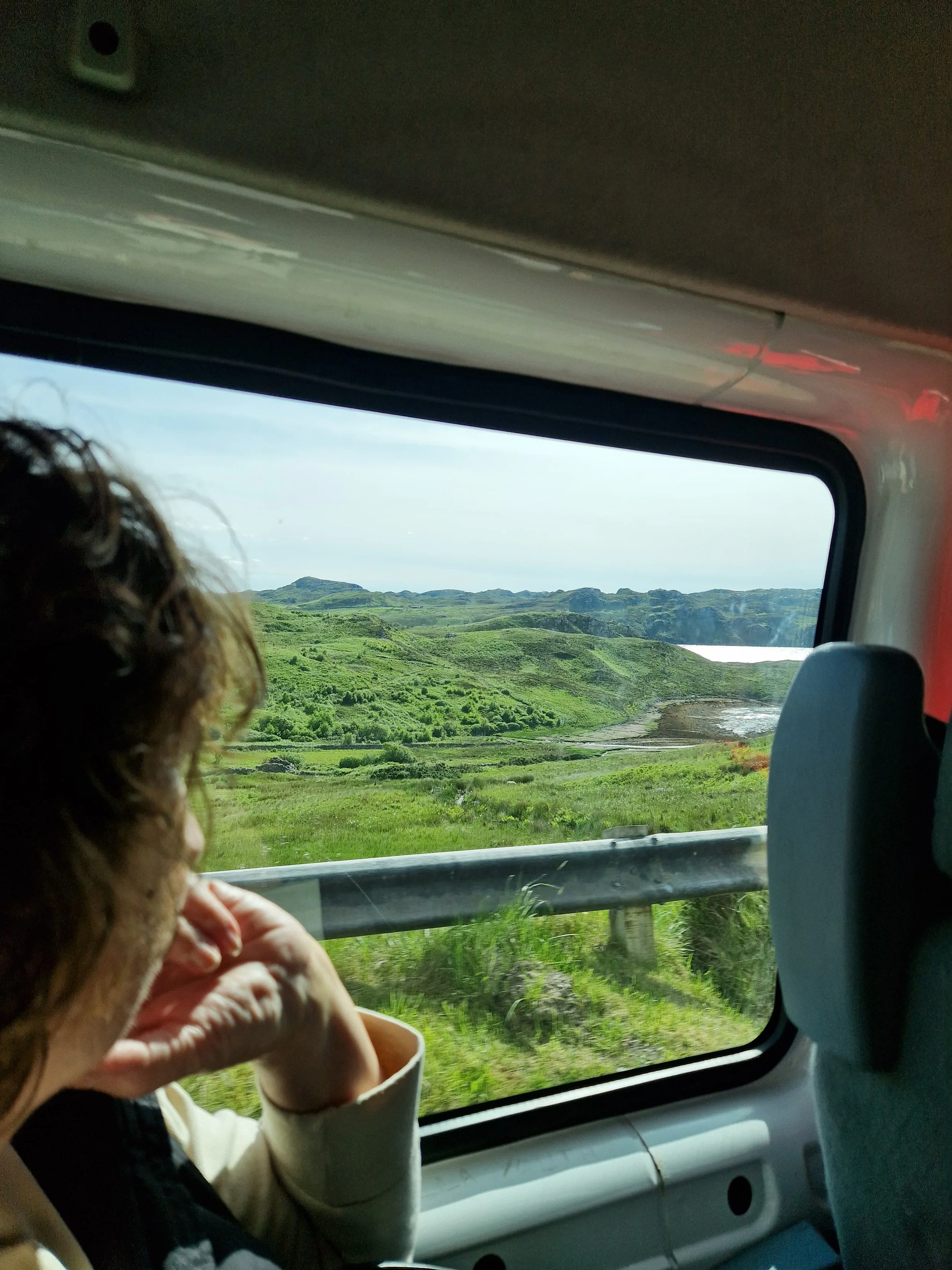 A woman gazing out a van window towards the Scottish landscape.