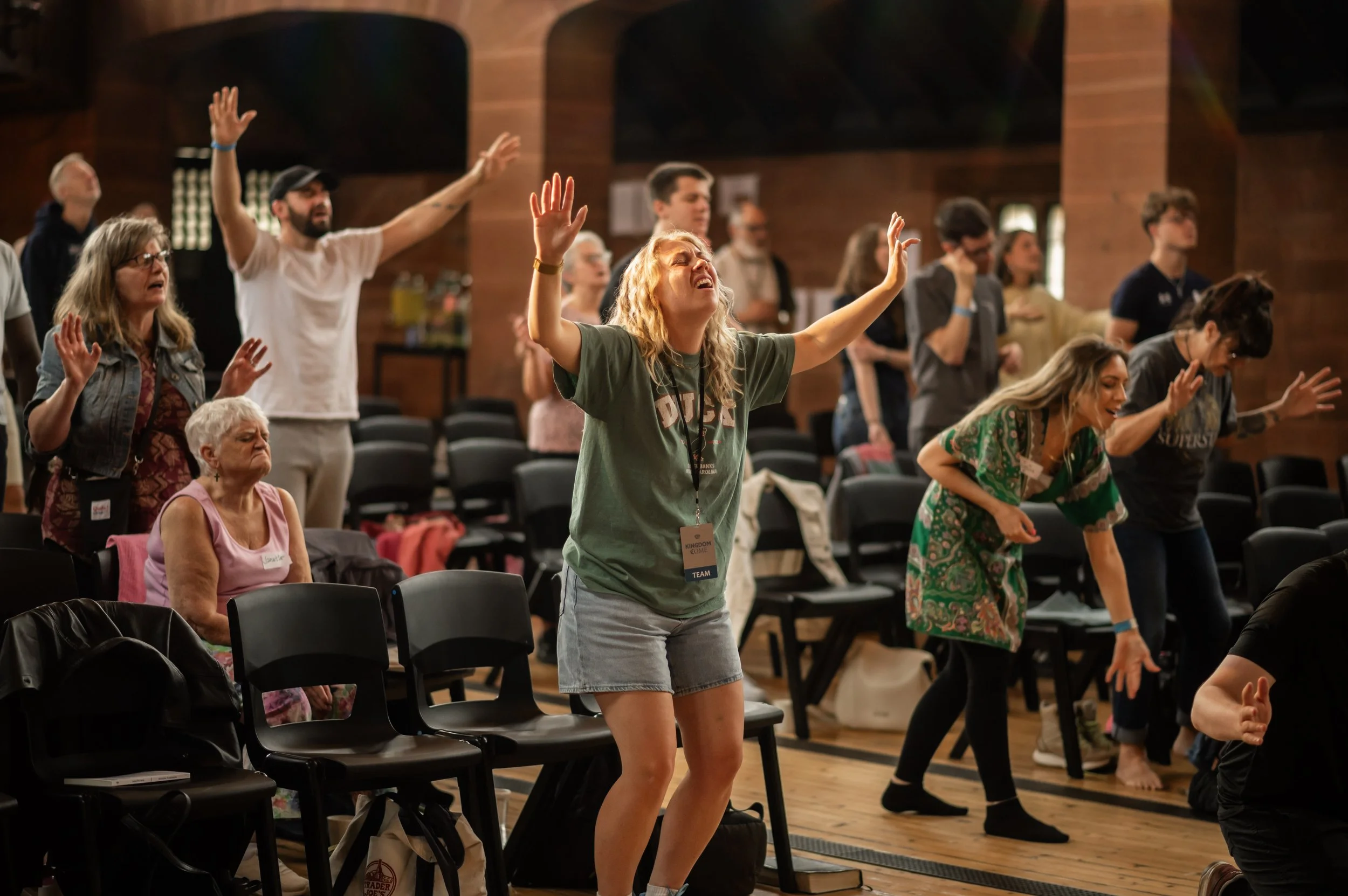 Focused on a woman worshipping at the front of the church rows, hands lifted, eyes closed, singing.