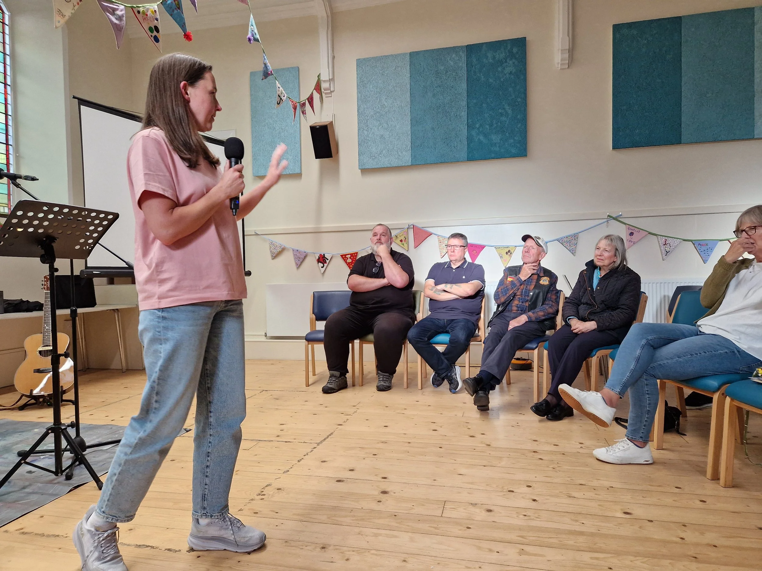A young woman speaking to a group of people sitting in a semi-circle in front of her,