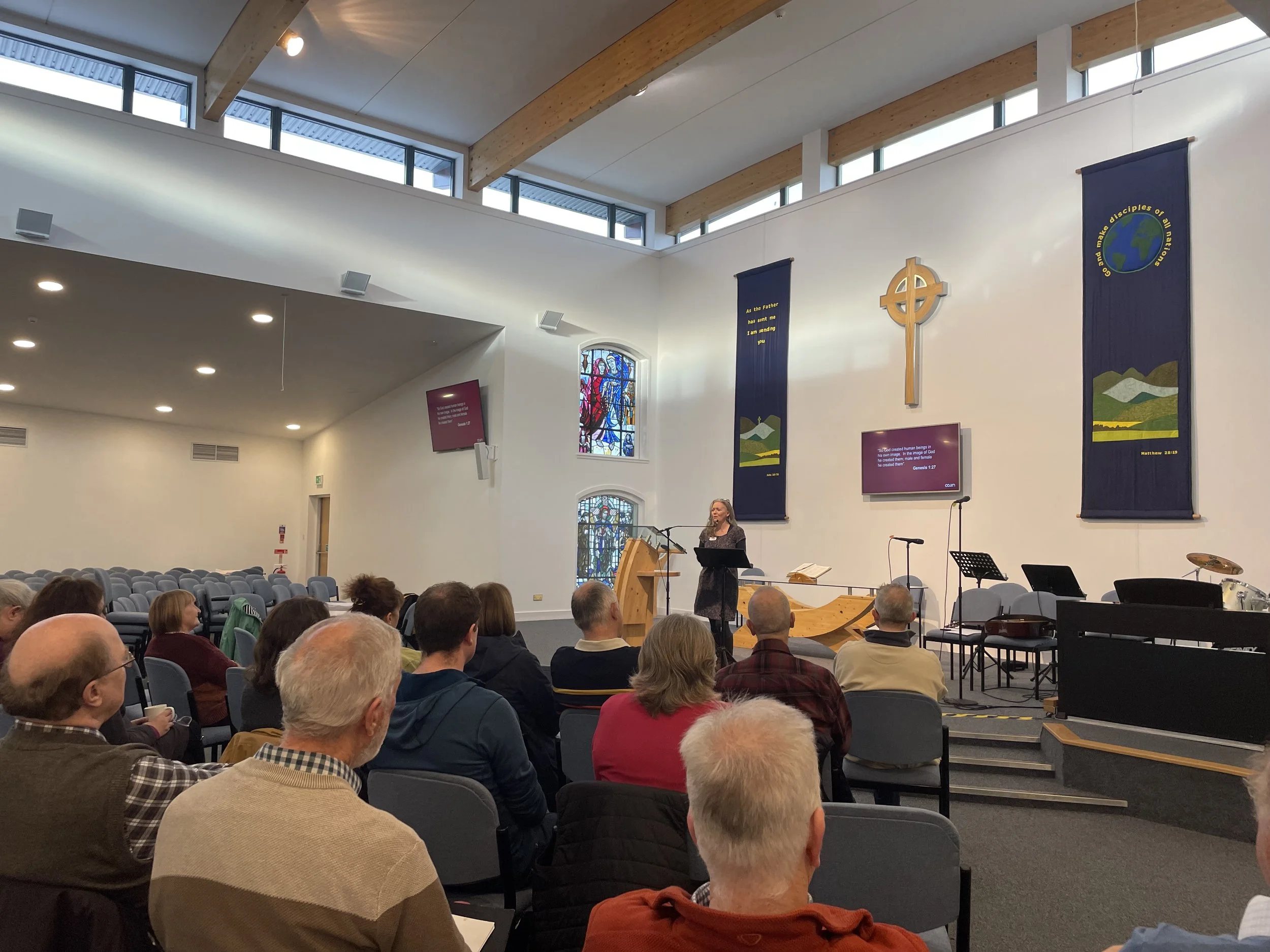 A teacher sharing at the front of a church building to a group of people.