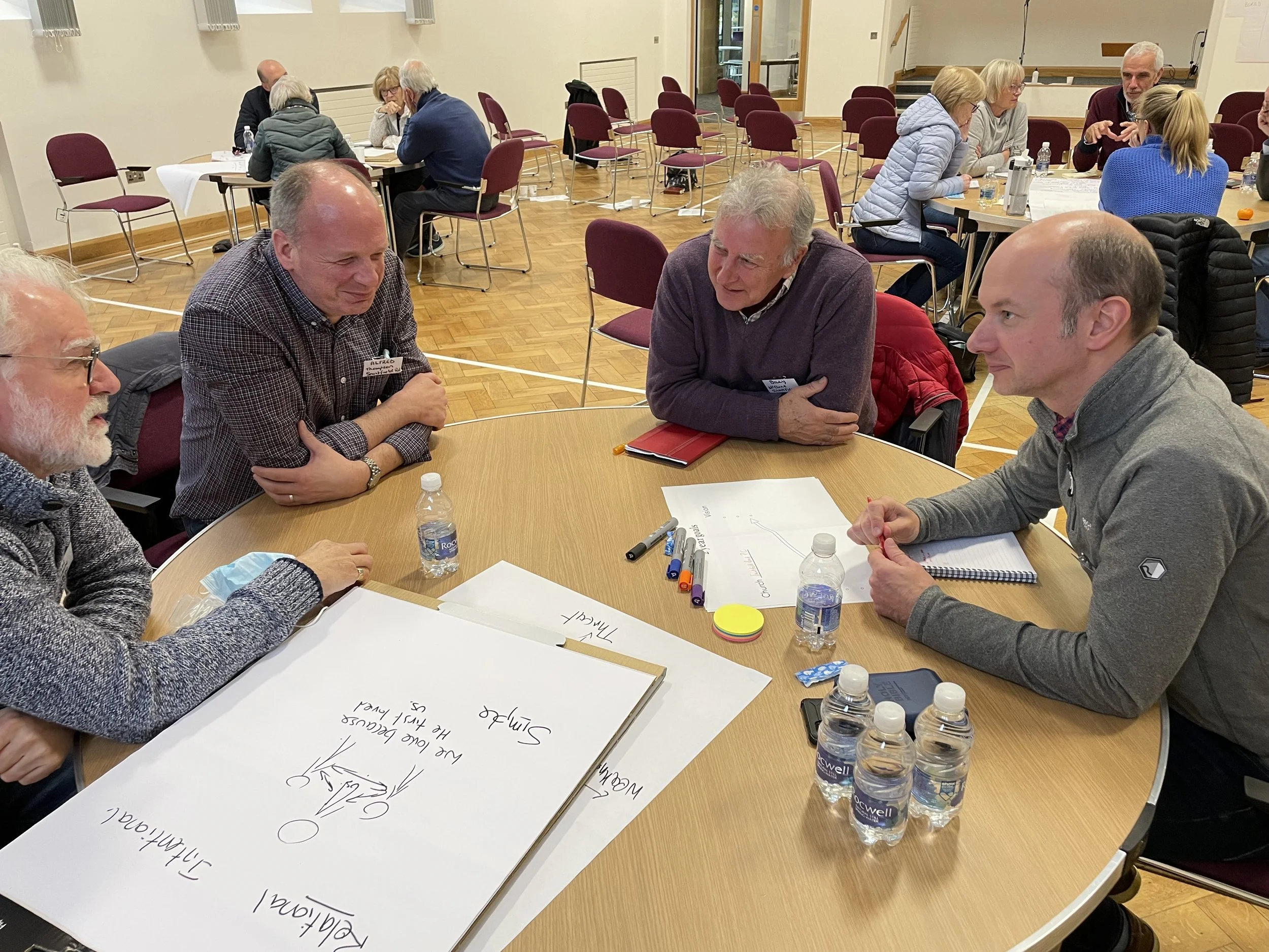 Four men sitting around a round table at a Learning Communities gathering, casting vision.