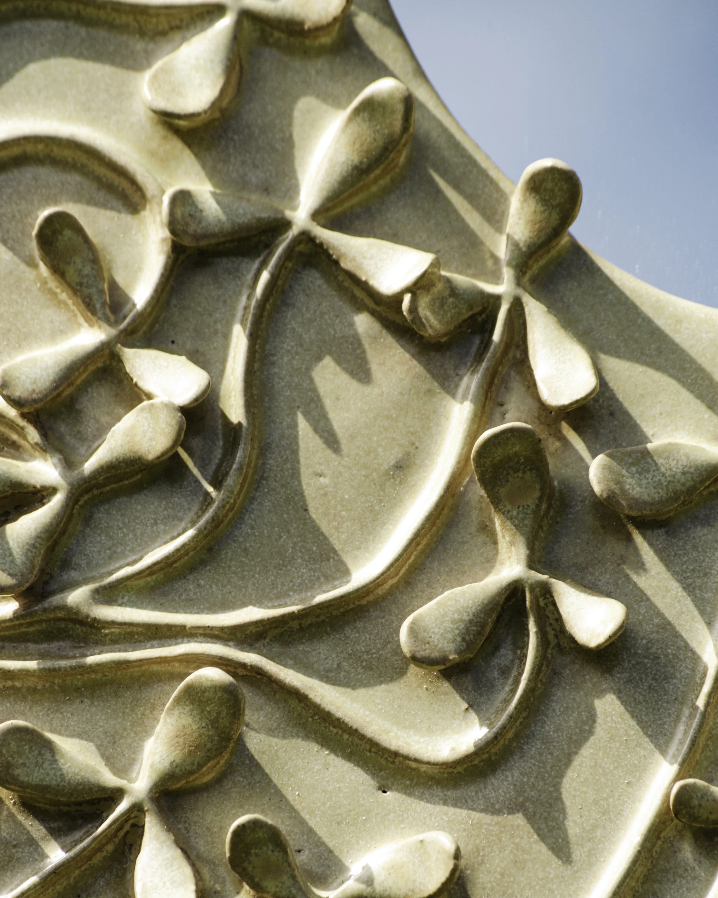 Close-up of a ceramic tile with a raised floral pattern featuring large, stylized flowers and leaves, with shadows cast by the relief design.