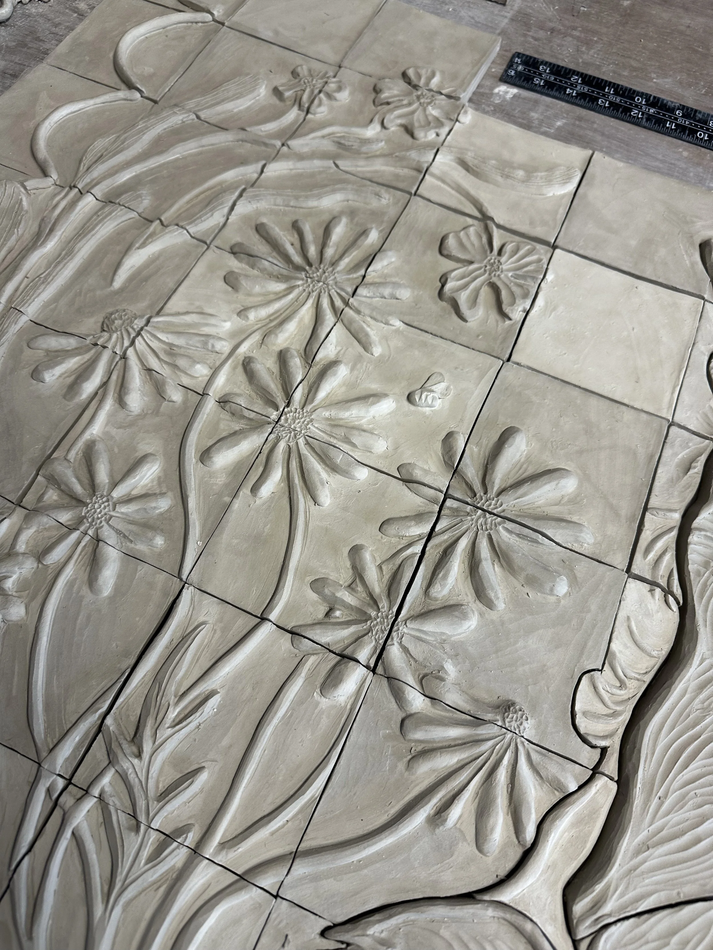 Carrelage en relief avec motifs floraux sculptés, comprenant des fleurs et des feuilles, avec une règle de mesure à côté.