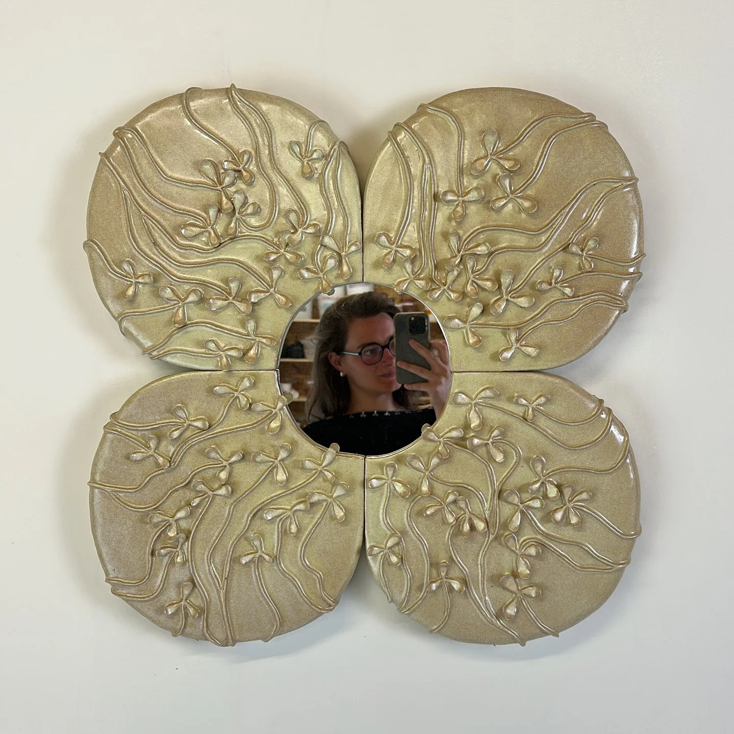 Decorative gold mirror shaped like a four-leaf clover with floral details, reflecting a woman taking a selfie.