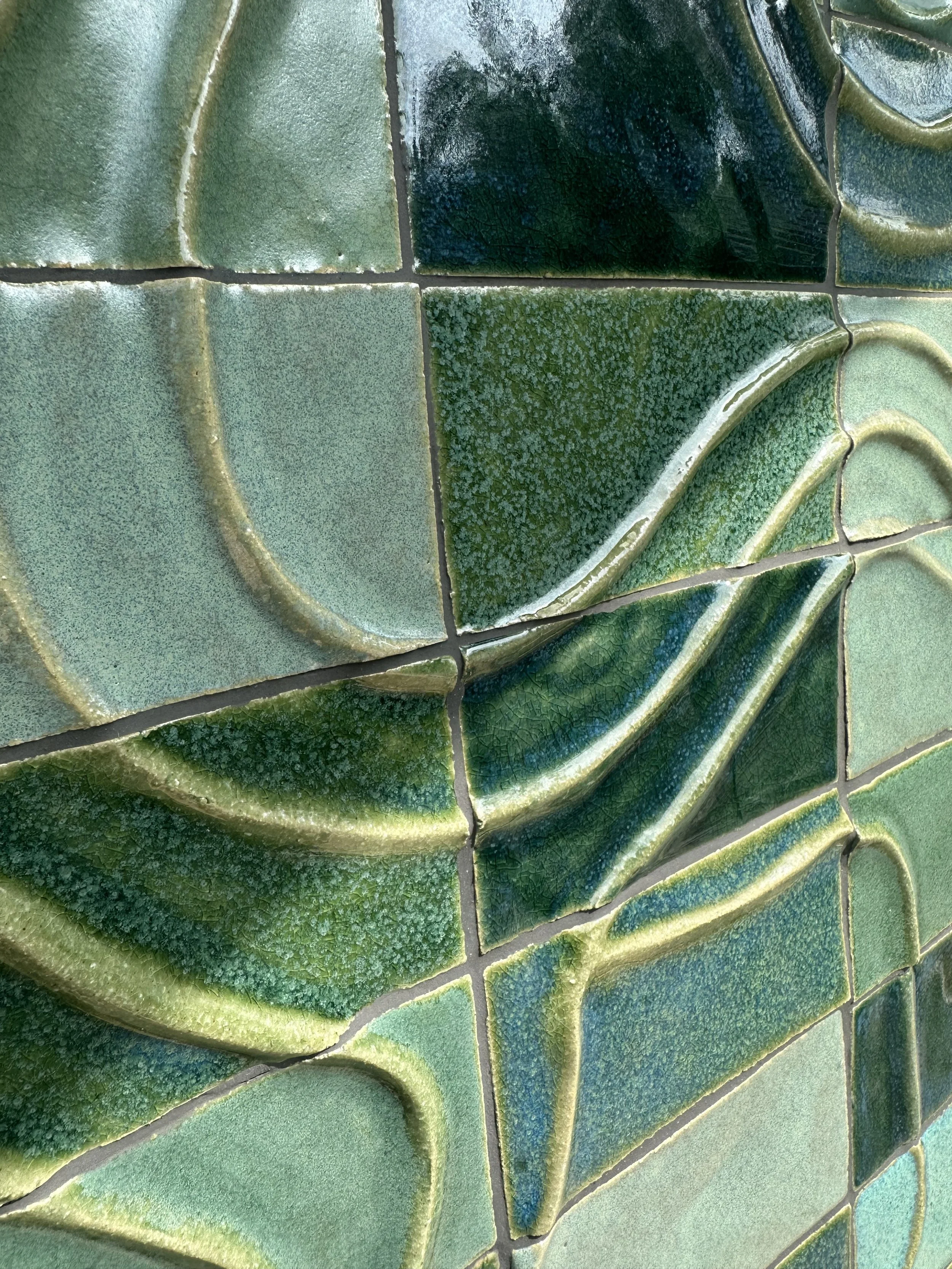 Zoom sur un mur en carreaux de céramique vert, avec des motifs floraux en relief et une surface brillante