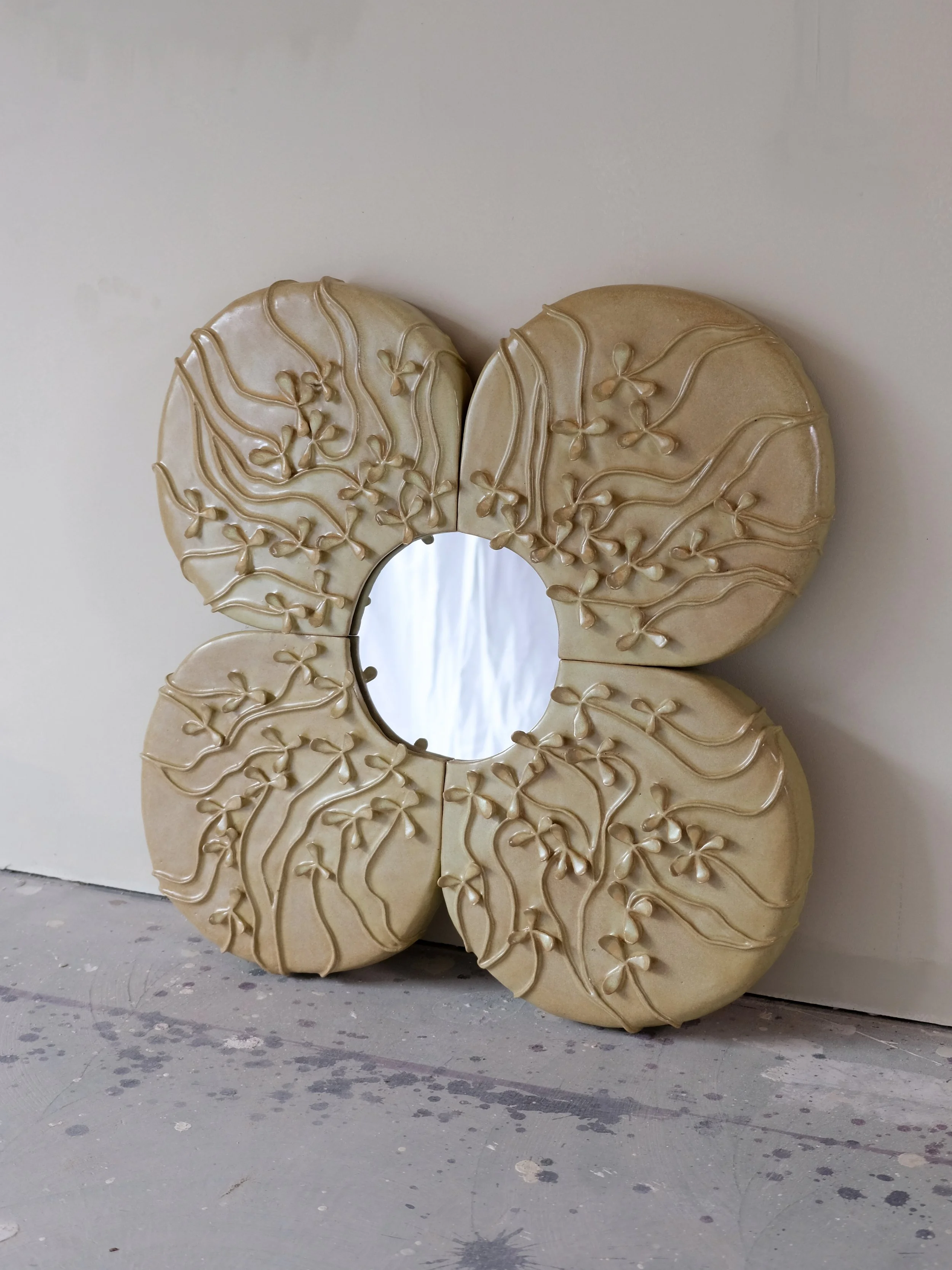 Decorative mirror with a heart-shaped frame featuring raised floral and vine motifs, leaning against a wall.