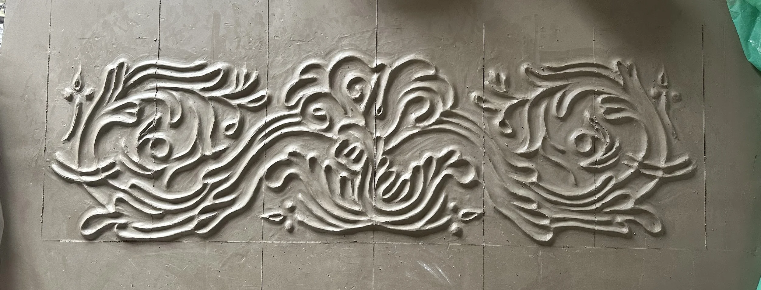 Une œuvre d'art en relief représentant deux poissons stylisés, faite en argile ou en plâtre, posée sur un sol en carrelage gris.