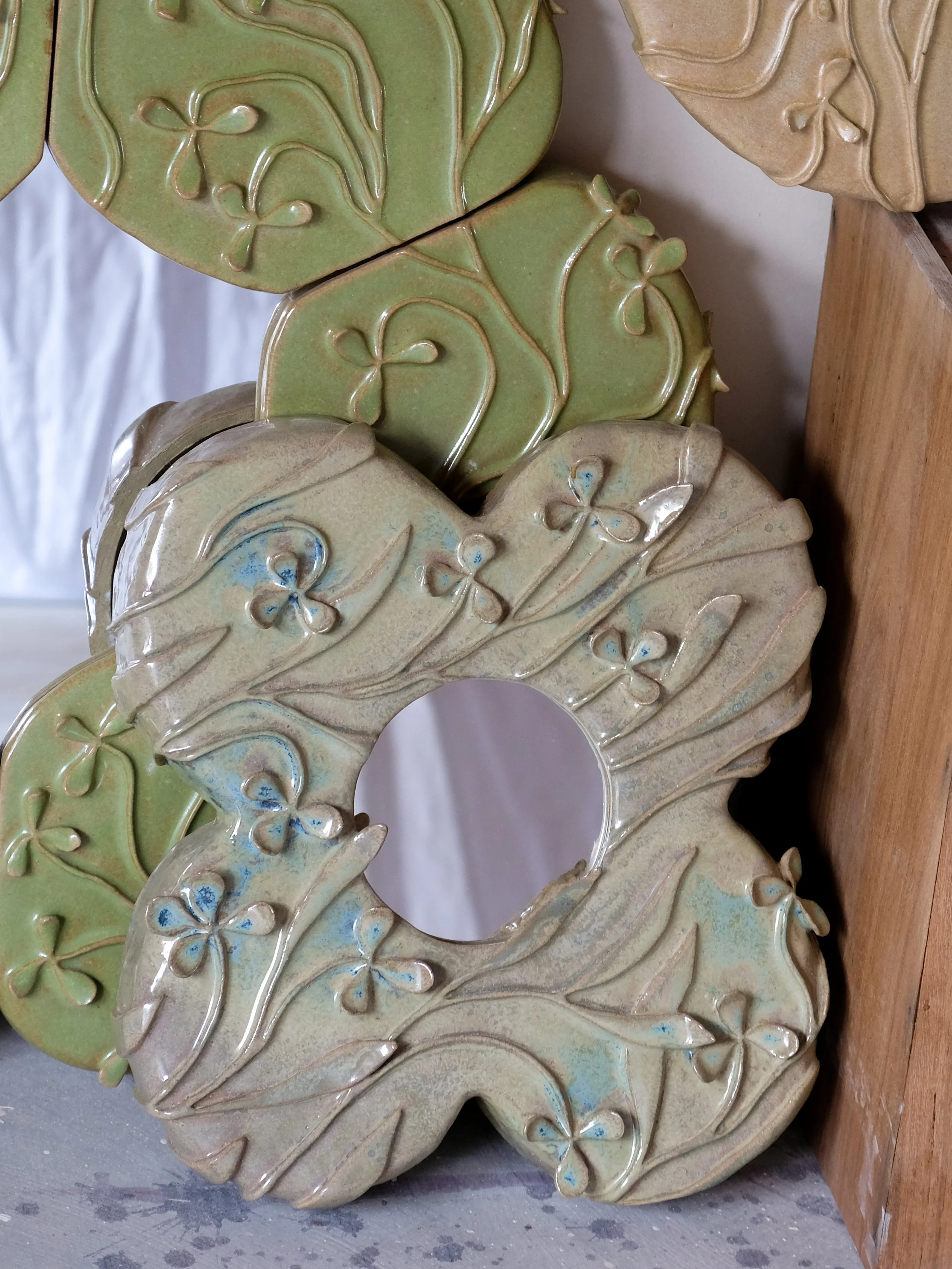 Decorative ceramic or pottery pieces with leaf and flower motifs, in shades of green, cream, and beige, displayed on a wooden surface.