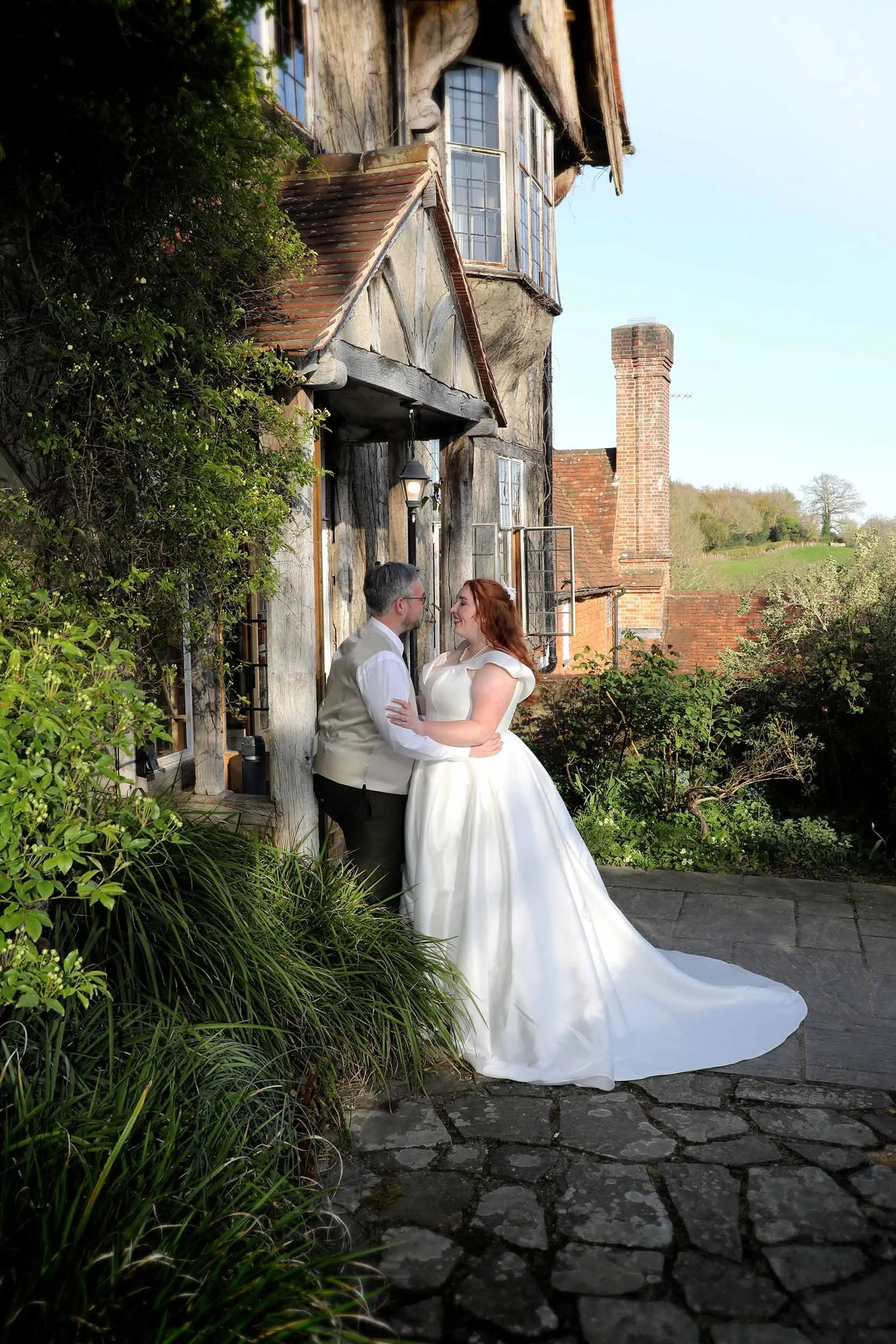 A bride and groom standing close together outdoors in front of Hoath house.
