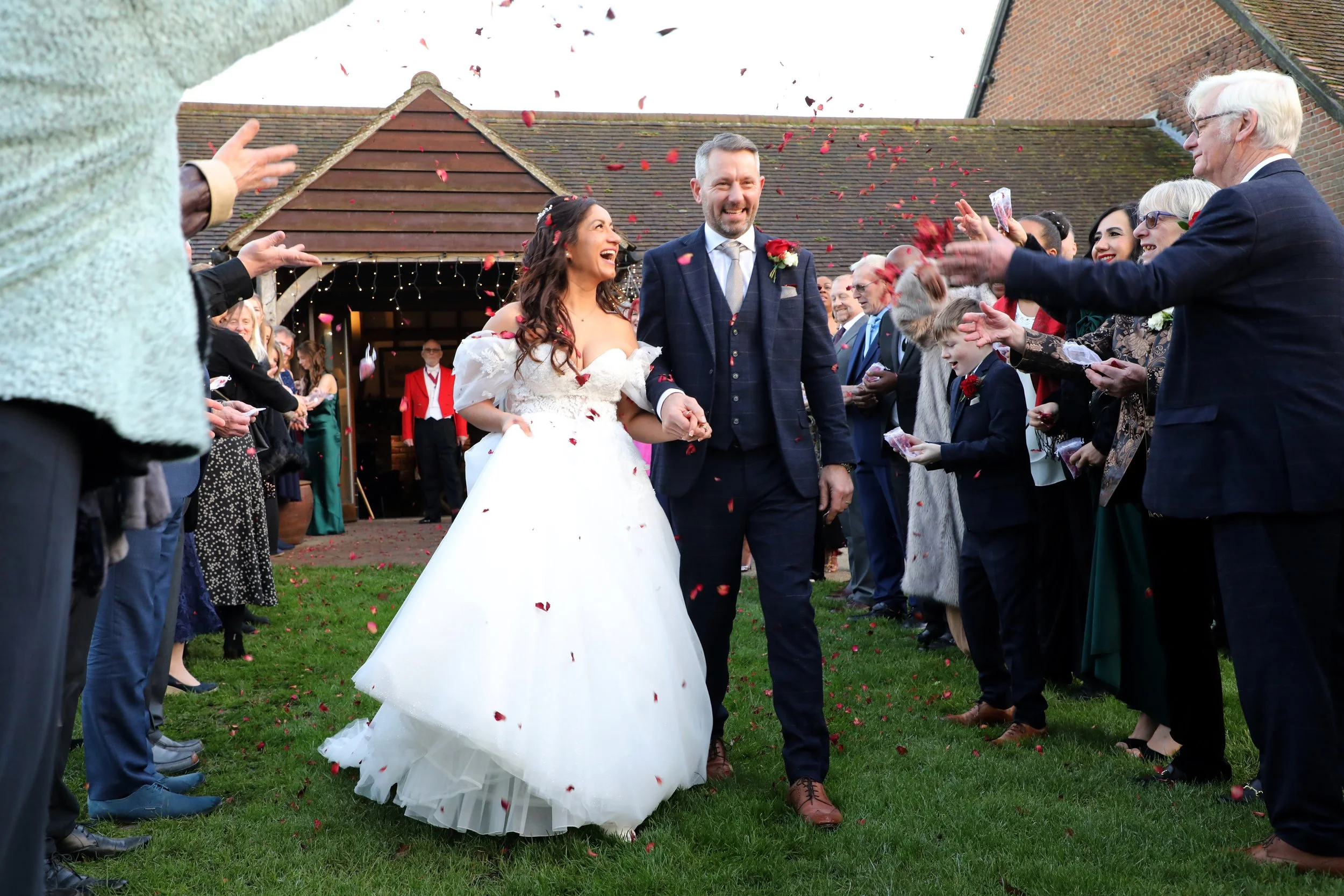 A newly married couple walking hand-in-hand through a line of friends and family celebrating with confetti at an outdoor wedding ceremony